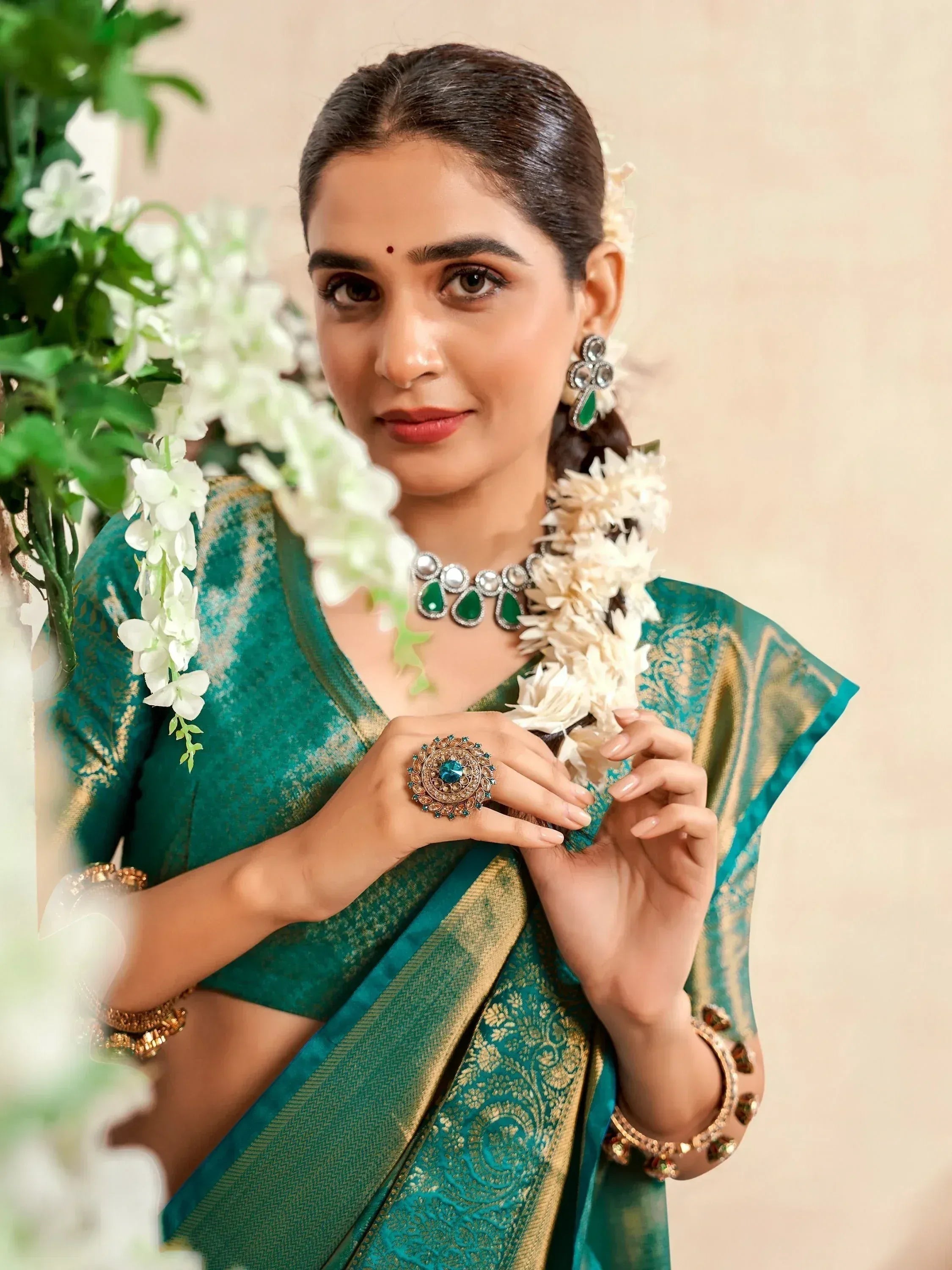 Woman in elegant green and gold saree with traditional jewelry and floral garland, perfect for Indian ethnic occasions.