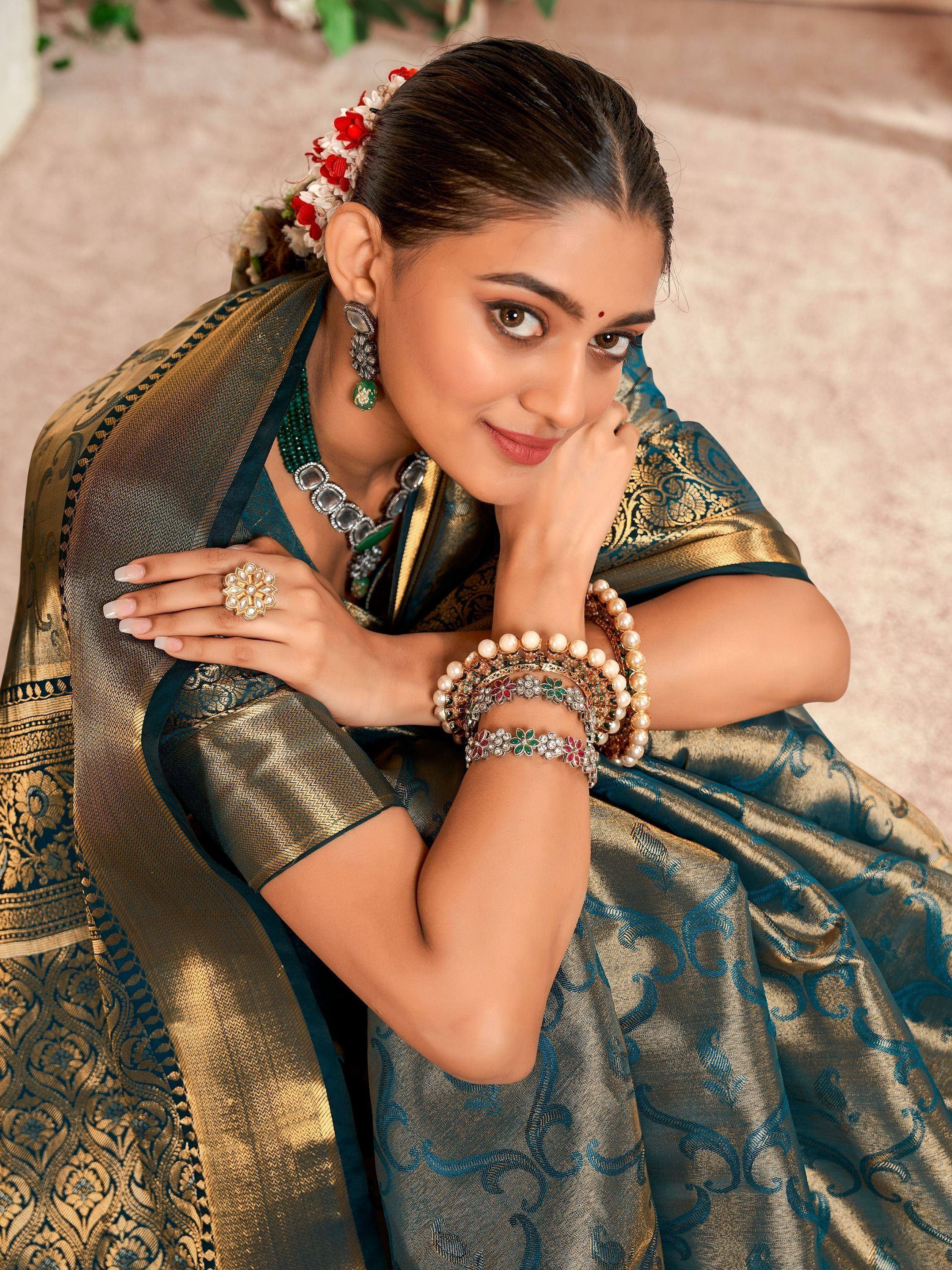 Woman in elegant teal and gold saree with floral hair accessory and traditional jewelry