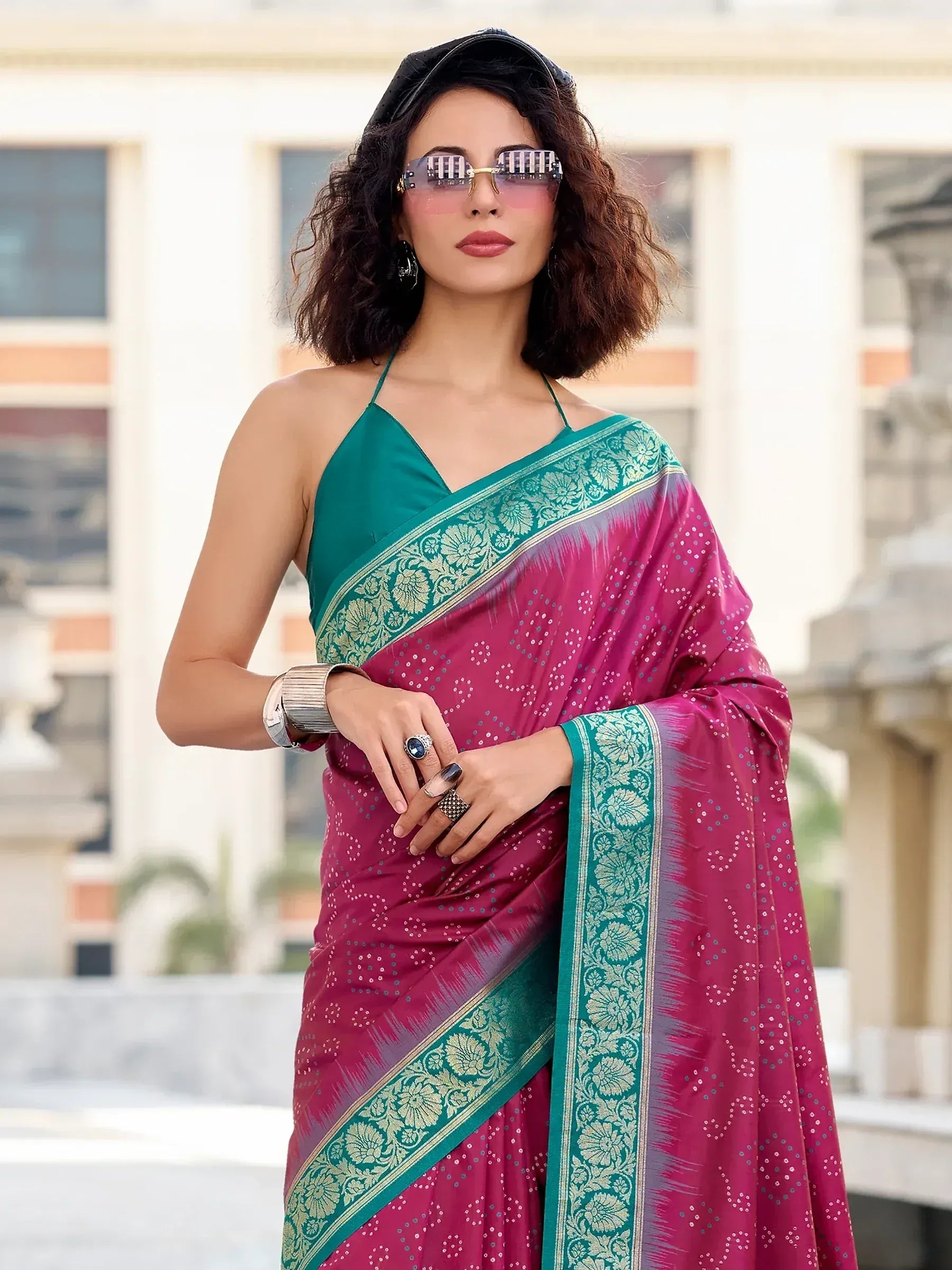 Woman in vibrant pink and green ethnic saree with floral border, stylish sunglasses, and modern accessories