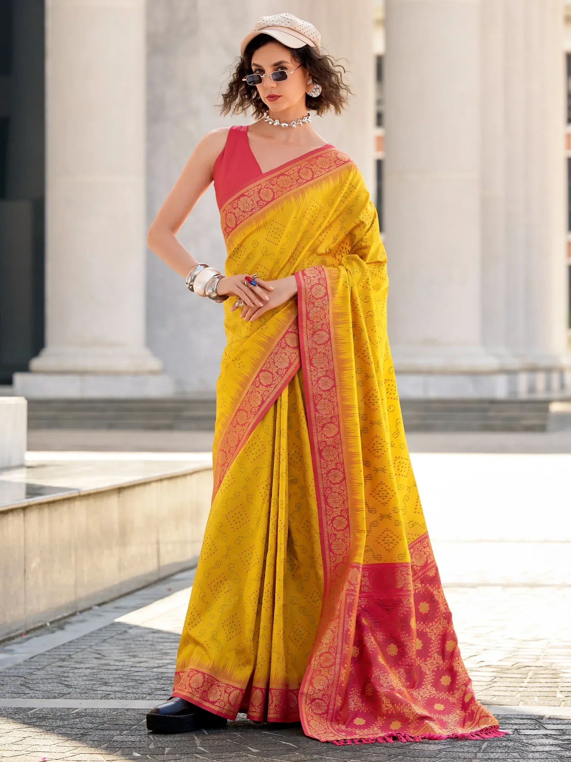 Yellow and pink designer saree with floral border, styled with cap and sunglasses for modern ethnic look