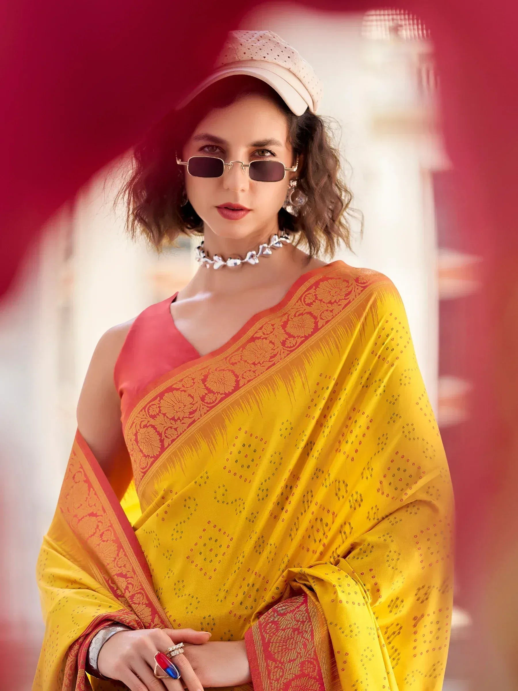 Yellow and red designer saree with floral border, paired with modern sunglasses and cap for ethnic fashion