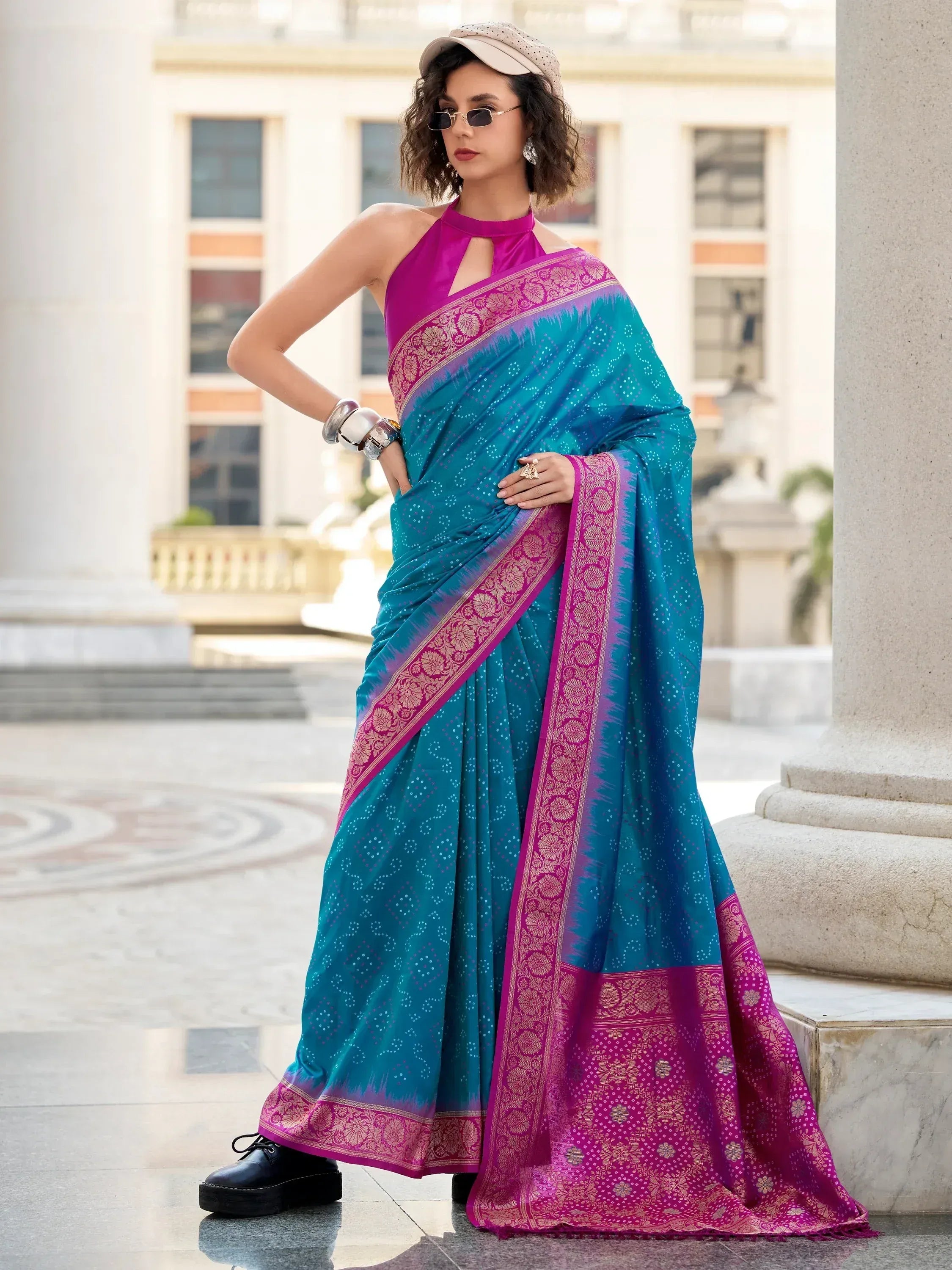 Teal and magenta designer saree with gold border, paired with halter neck blouse, styled with cap and sunglasses
