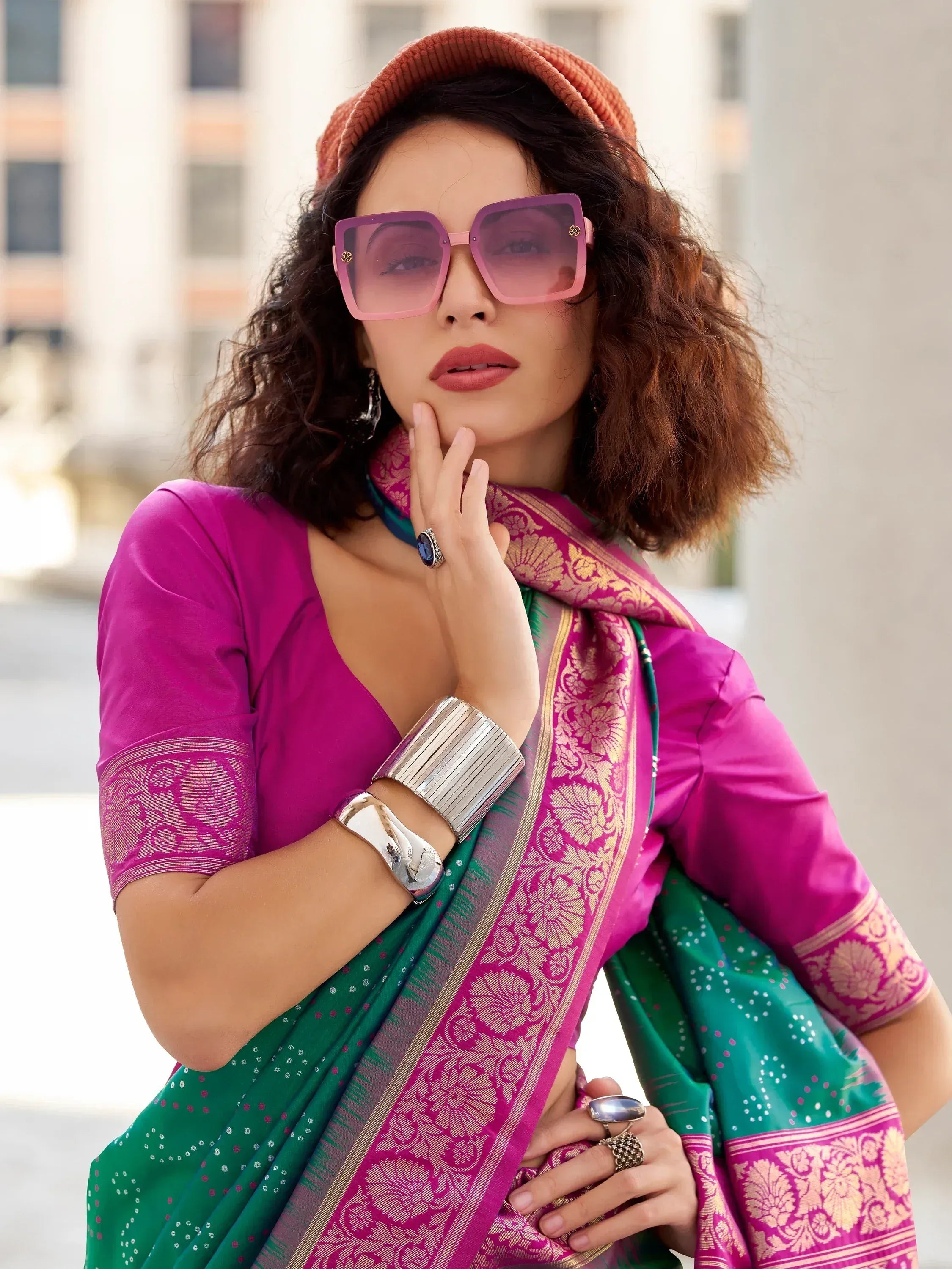 Woman in vibrant green and pink ethnic saree with gold border, styled with beret and sunglasses