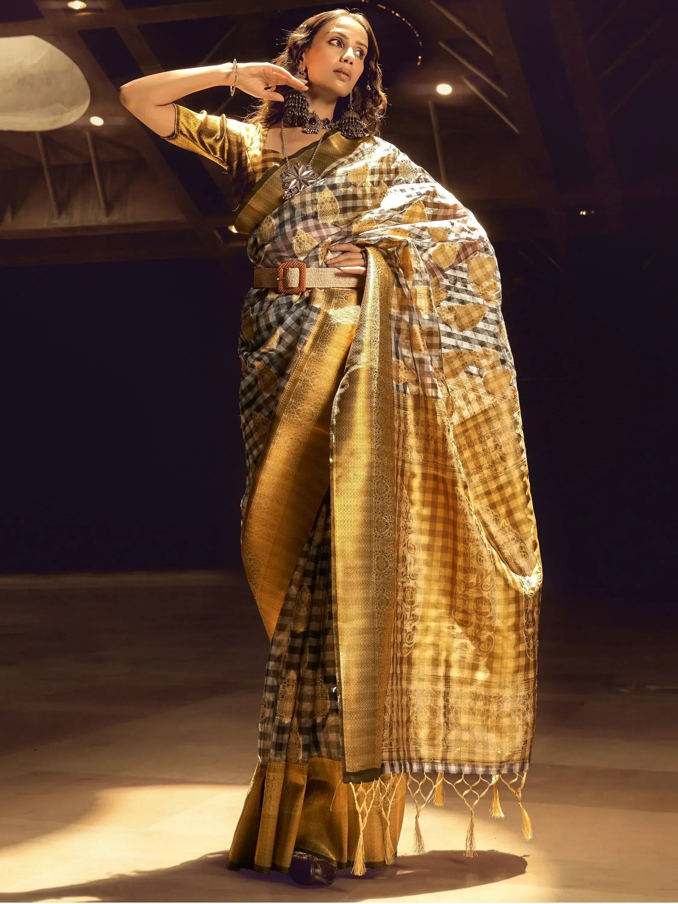 Woman in elegant gold and checkered saree with intricate patterns, styled with belt and statement jewelry