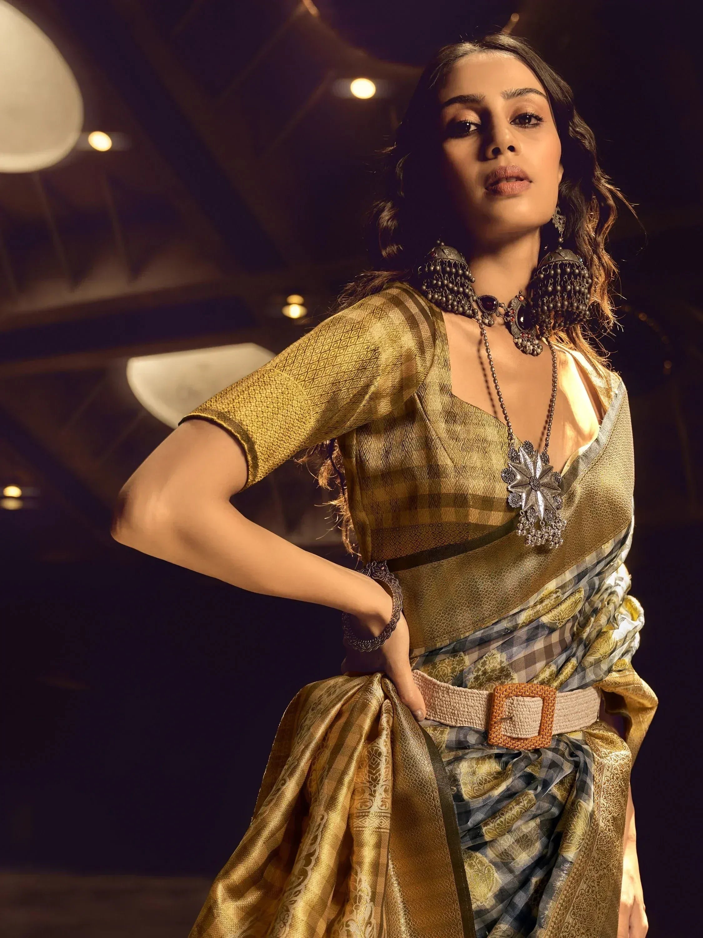 Woman in golden ethnic saree with checkered pallu, statement jewelry, and belt for festive occasions