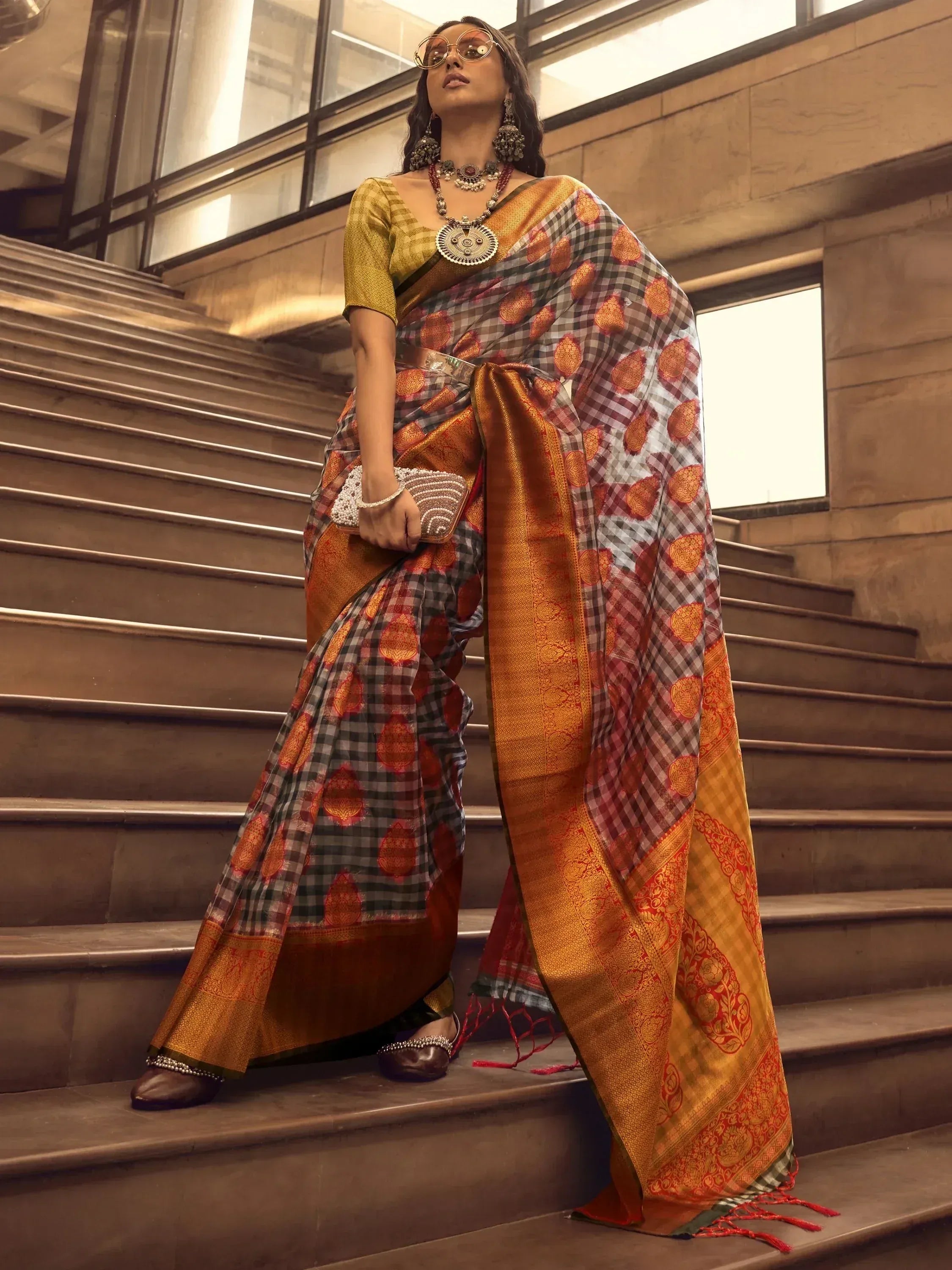 Woman in designer saree with checkered and floral print, ethnic jewelry, standing on stairs
