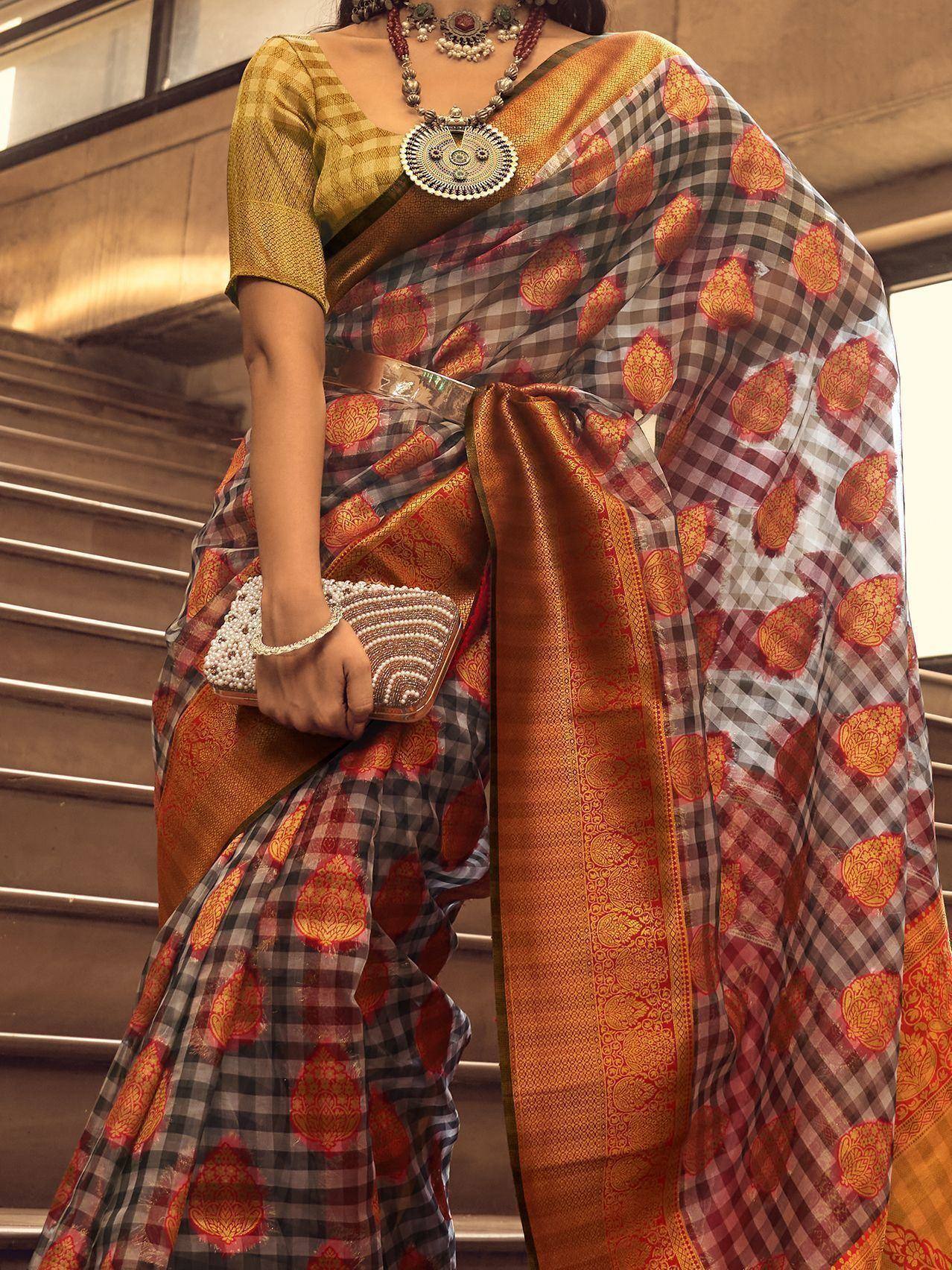 Woman in ethnic saree with checkered print, gold blouse, and traditional jewelry, holding beaded clutch