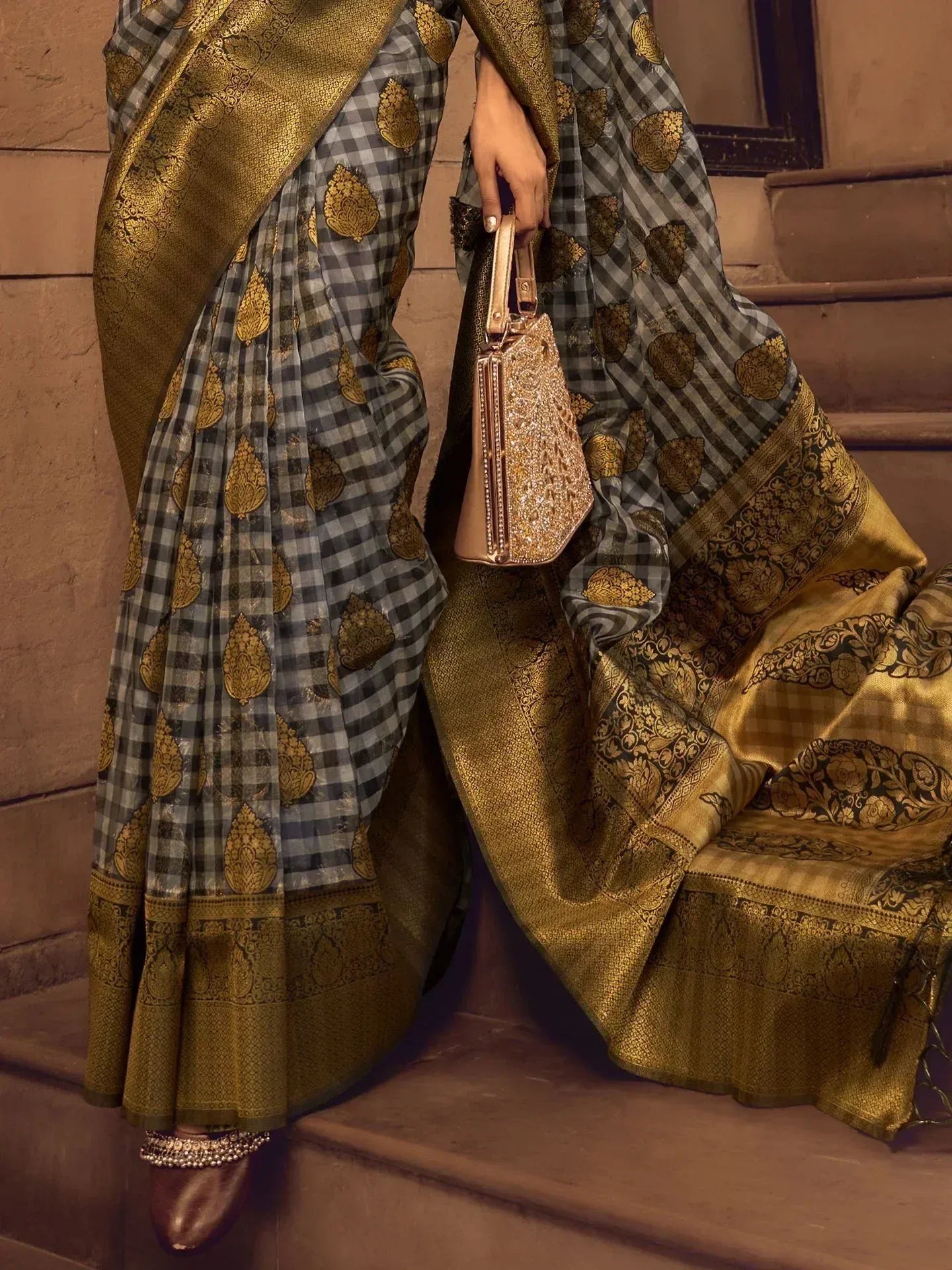 Grey and gold checkered saree with intricate zari border, paired with embellished clutch and traditional footwear