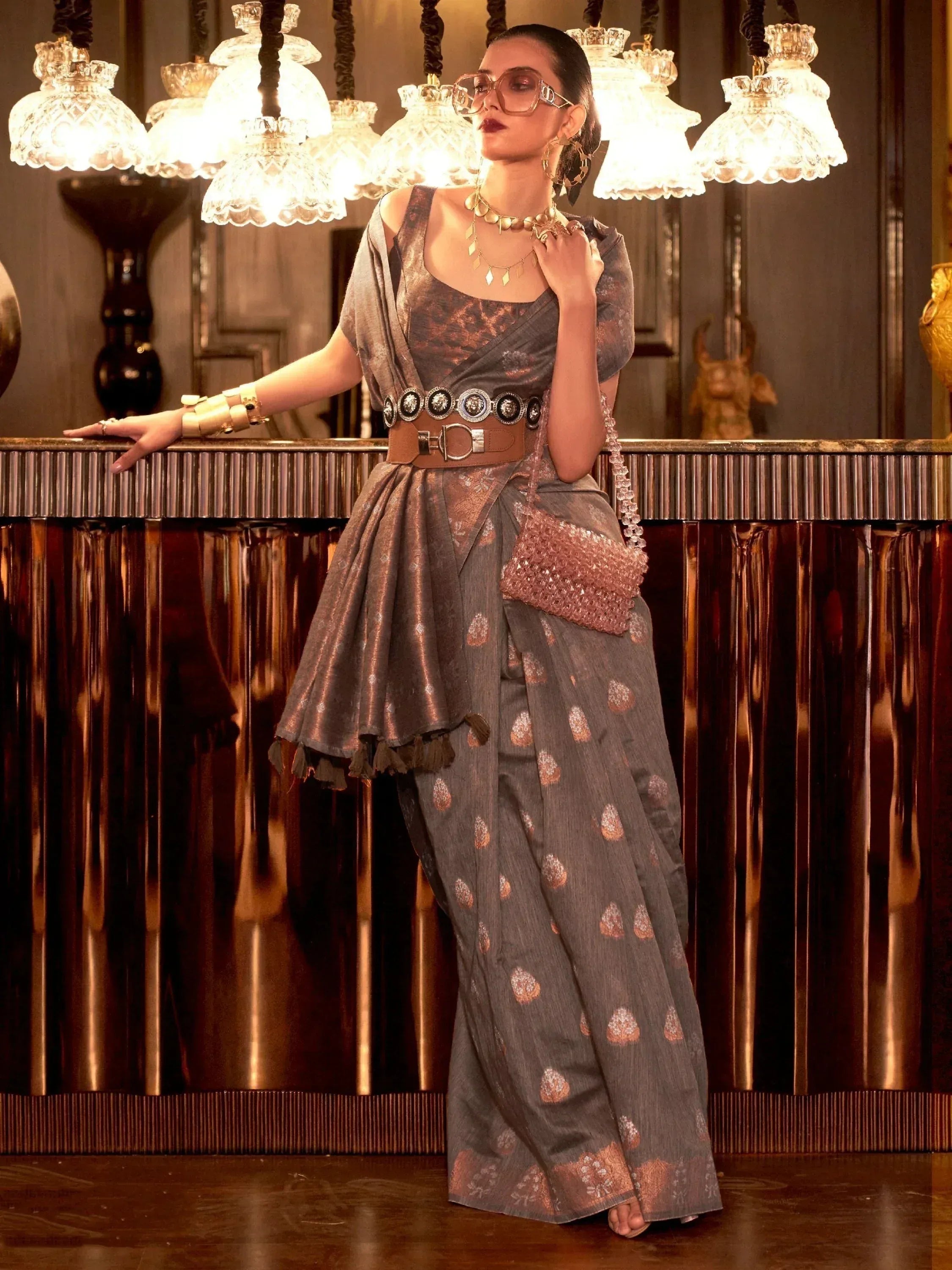Stylish grey printed saree with wide belt, statement jewelry, and crystal bag for ethnic wear