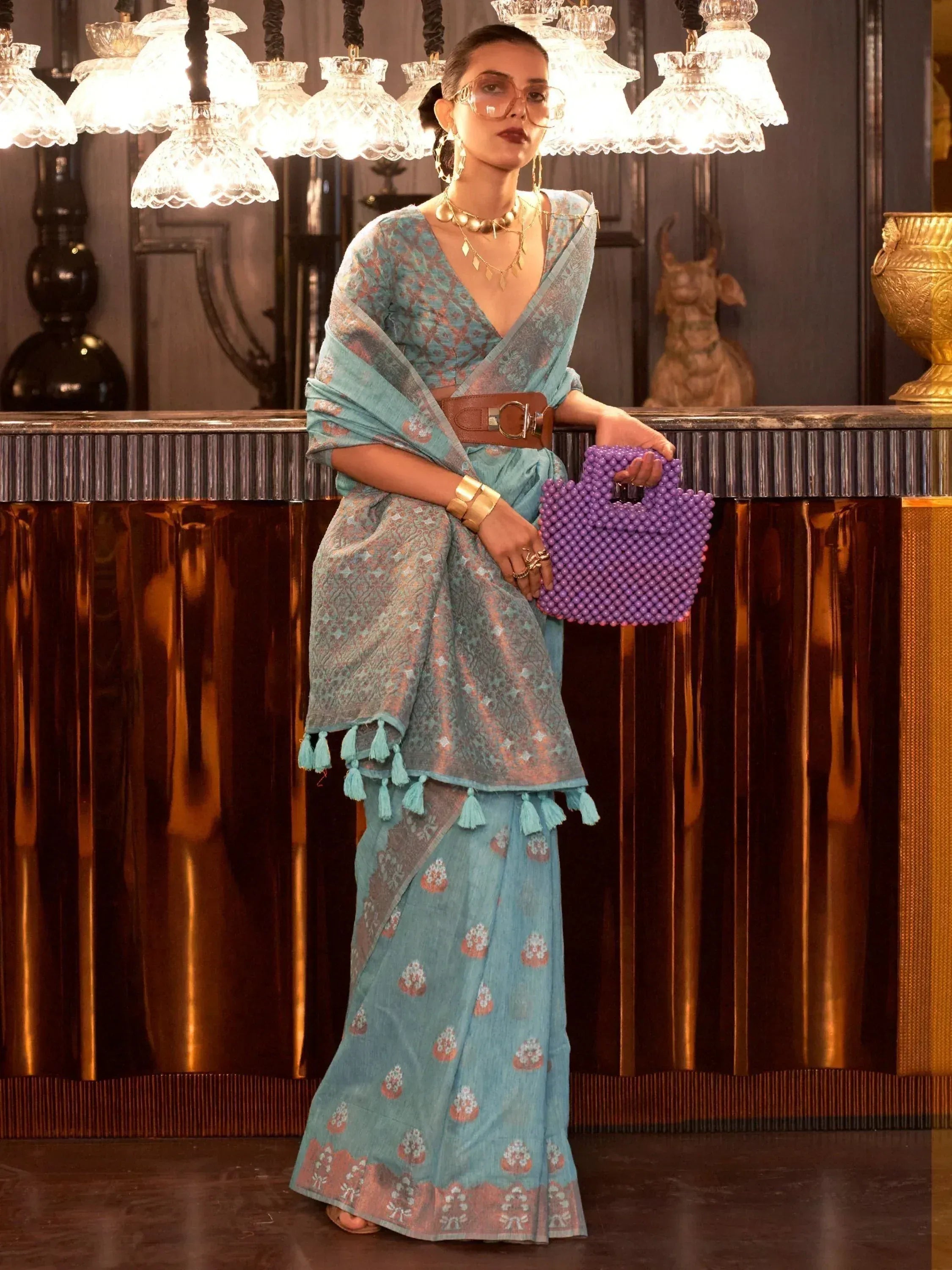 Stylish blue printed saree with tassels, gold jewelry, and purple beaded bag for ethnic wear
