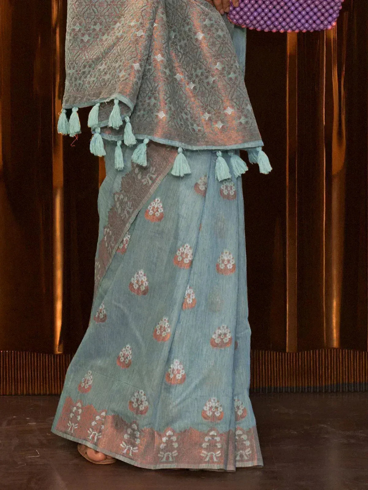 Light blue printed saree with tassel border, paired with matching blouse and purple beaded clutch