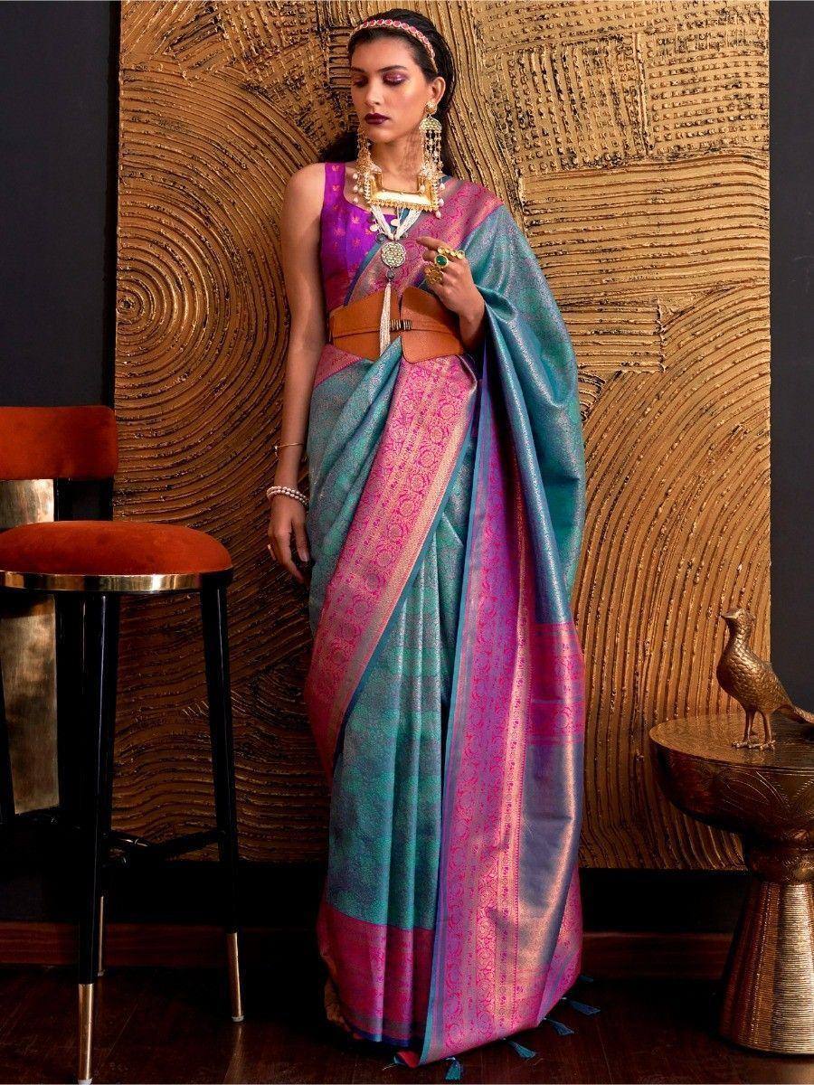 Teal and pink designer saree with gold border, paired with purple blouse and statement jewelry