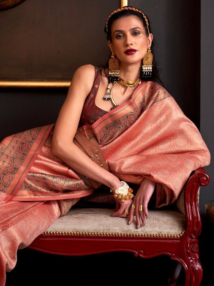 Elegant woman in peach designer saree with gold jewelry, seated on ornate chair