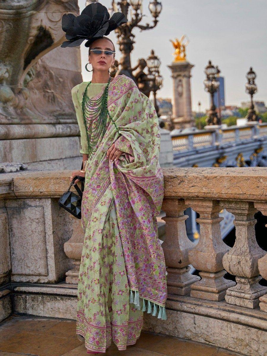 Woman in floral green and pink saree with tassels, styled with statement hat and beads, on ornate bridge