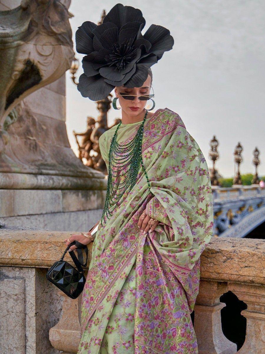 Stylish woman in floral green saree with black floral hat, sunglasses, and green beads, leaning on stone railing