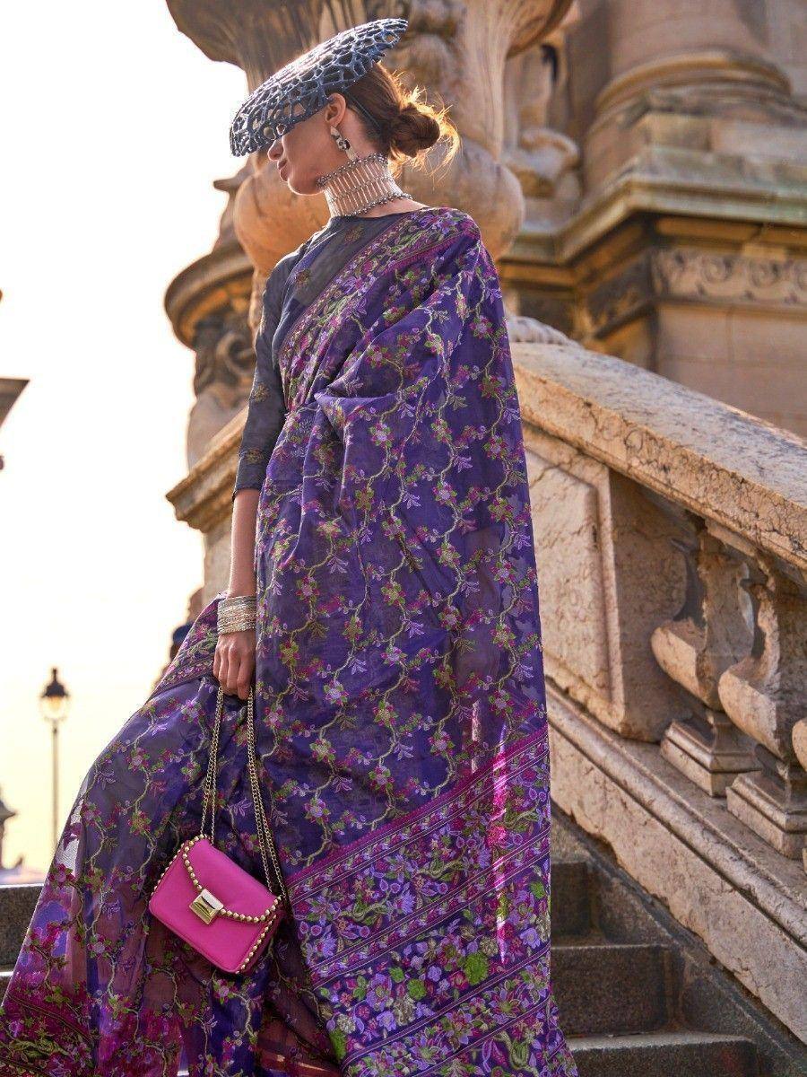 Purple floral saree with intricate embroidery, paired with a stylish hat and pink handbag, perfect for ethnic occasions.