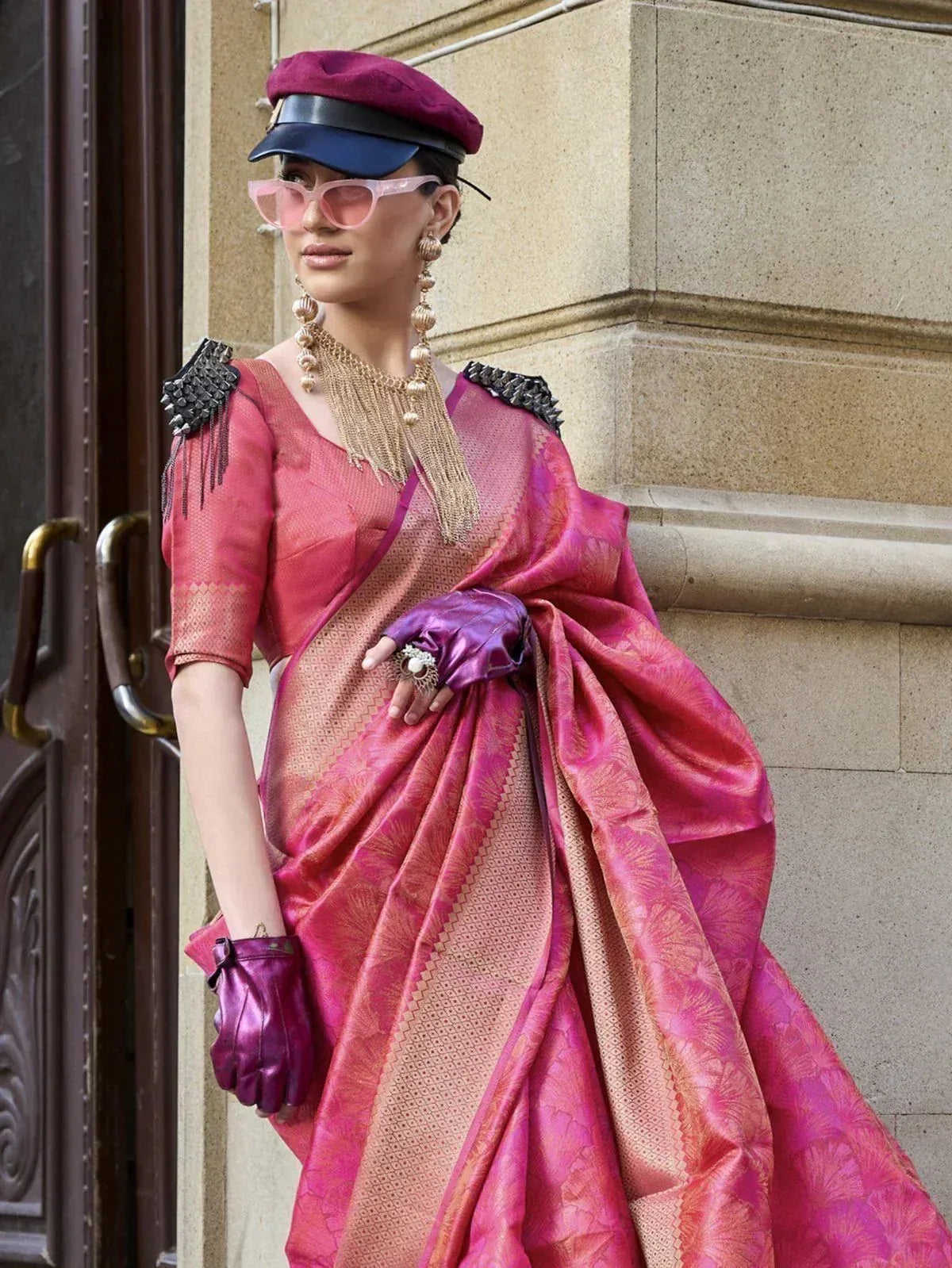 Stylish pink designer saree with gold patterns, paired with purple gloves and cap, perfect for ethnic fashion events.