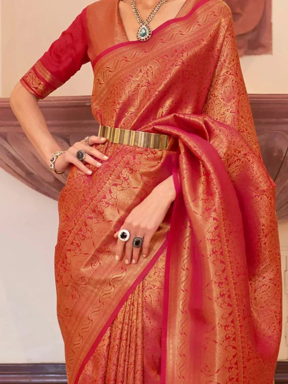 Orange and pink designer saree with gold paisley print, paired with statement jewelry and a gold belt