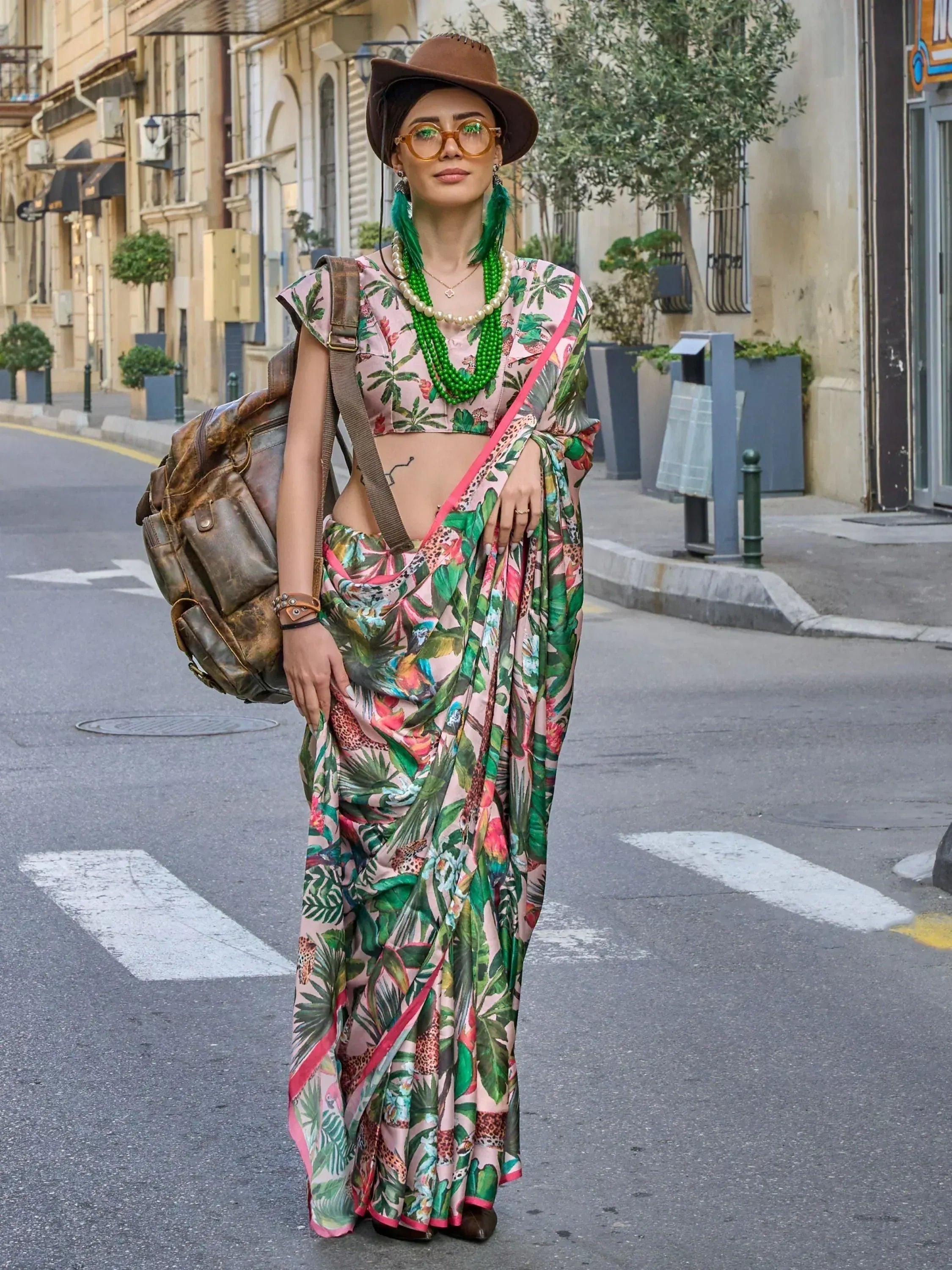 Woman in floral print saree with green beads, hat, and backpack on city street