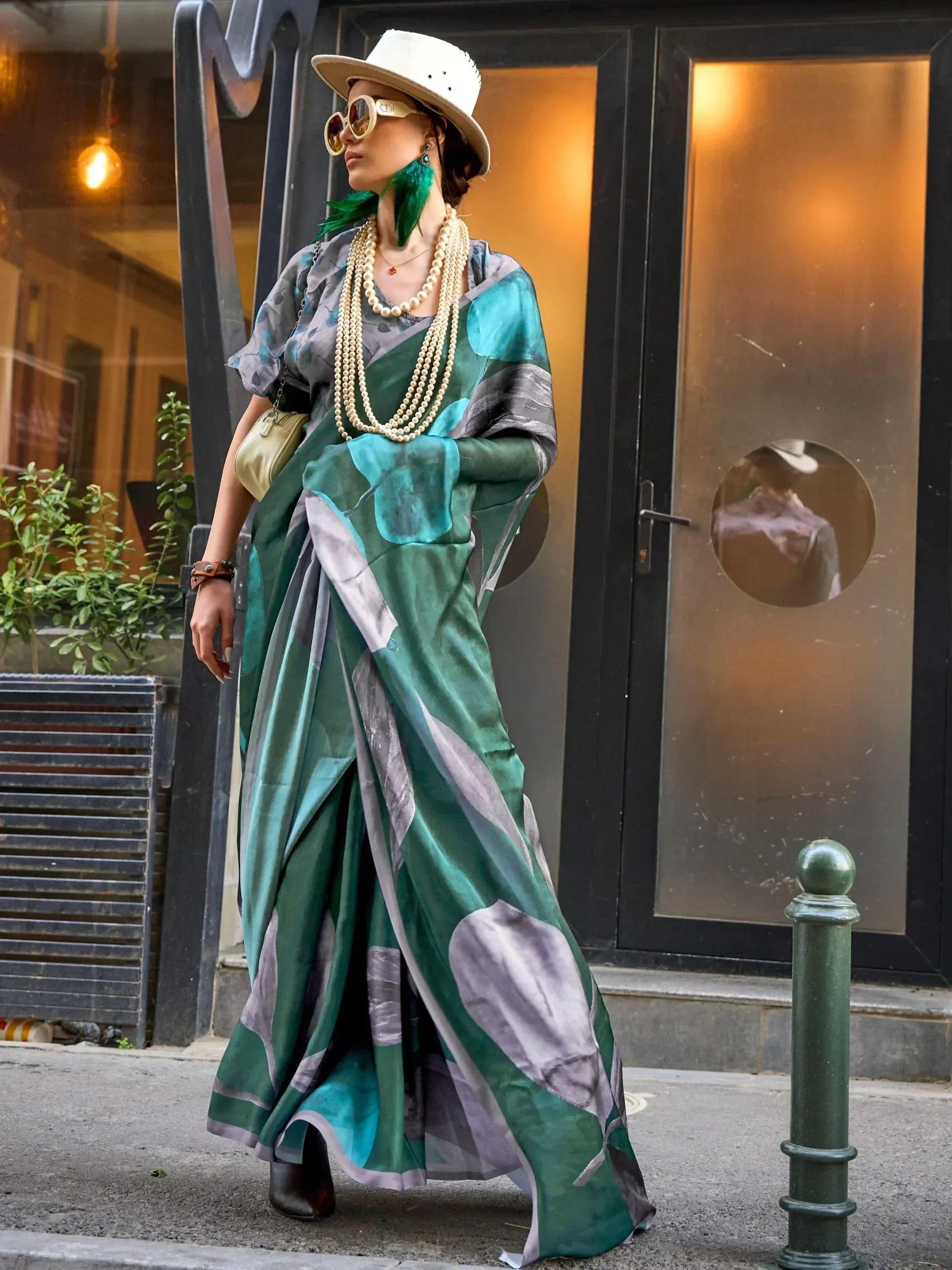 Woman in green and grey printed saree with pearl necklaces, white hat, and feather earrings, street style