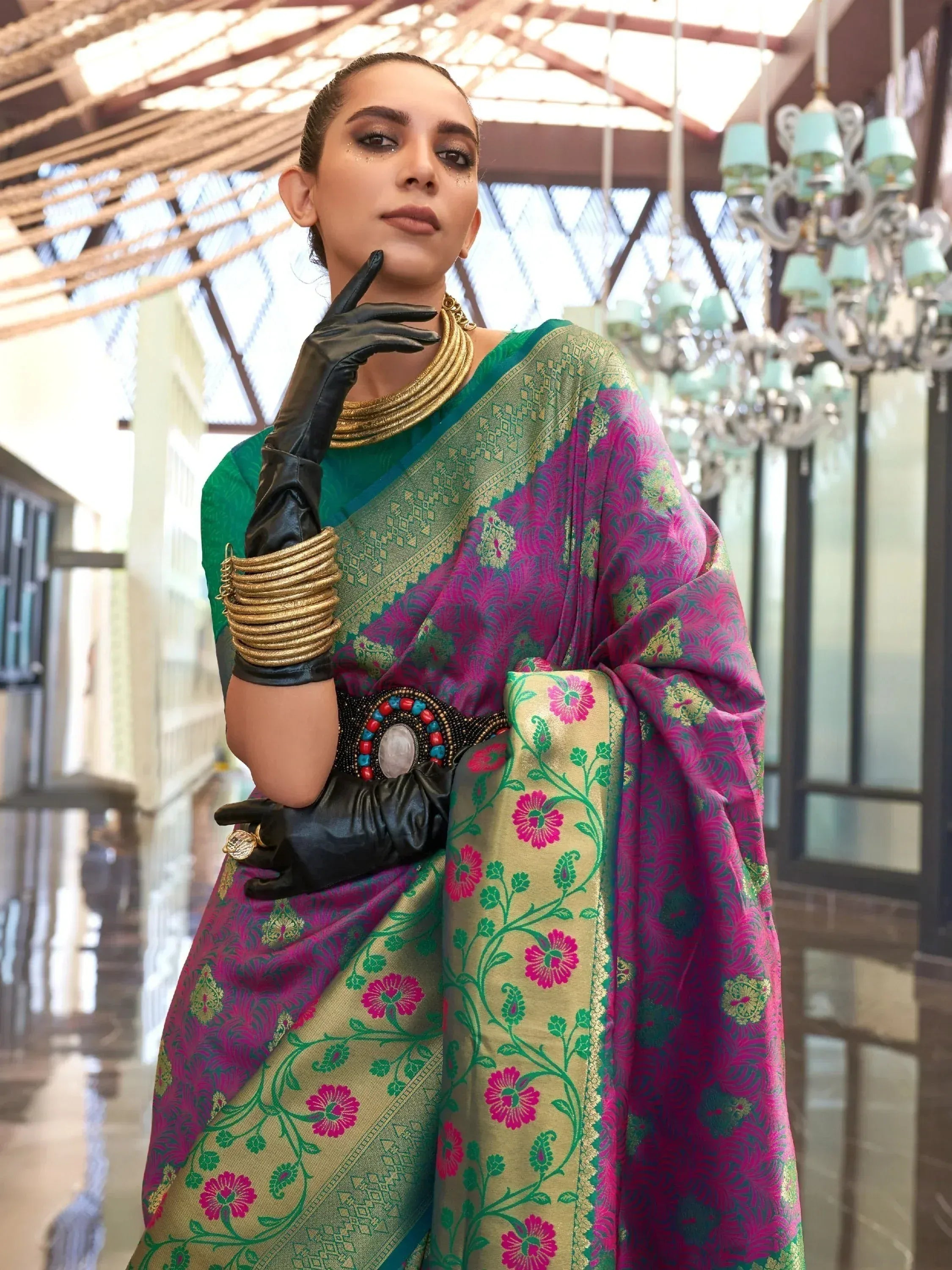 Woman in vibrant pink and green floral saree with gold border, black gloves, and statement jewelry