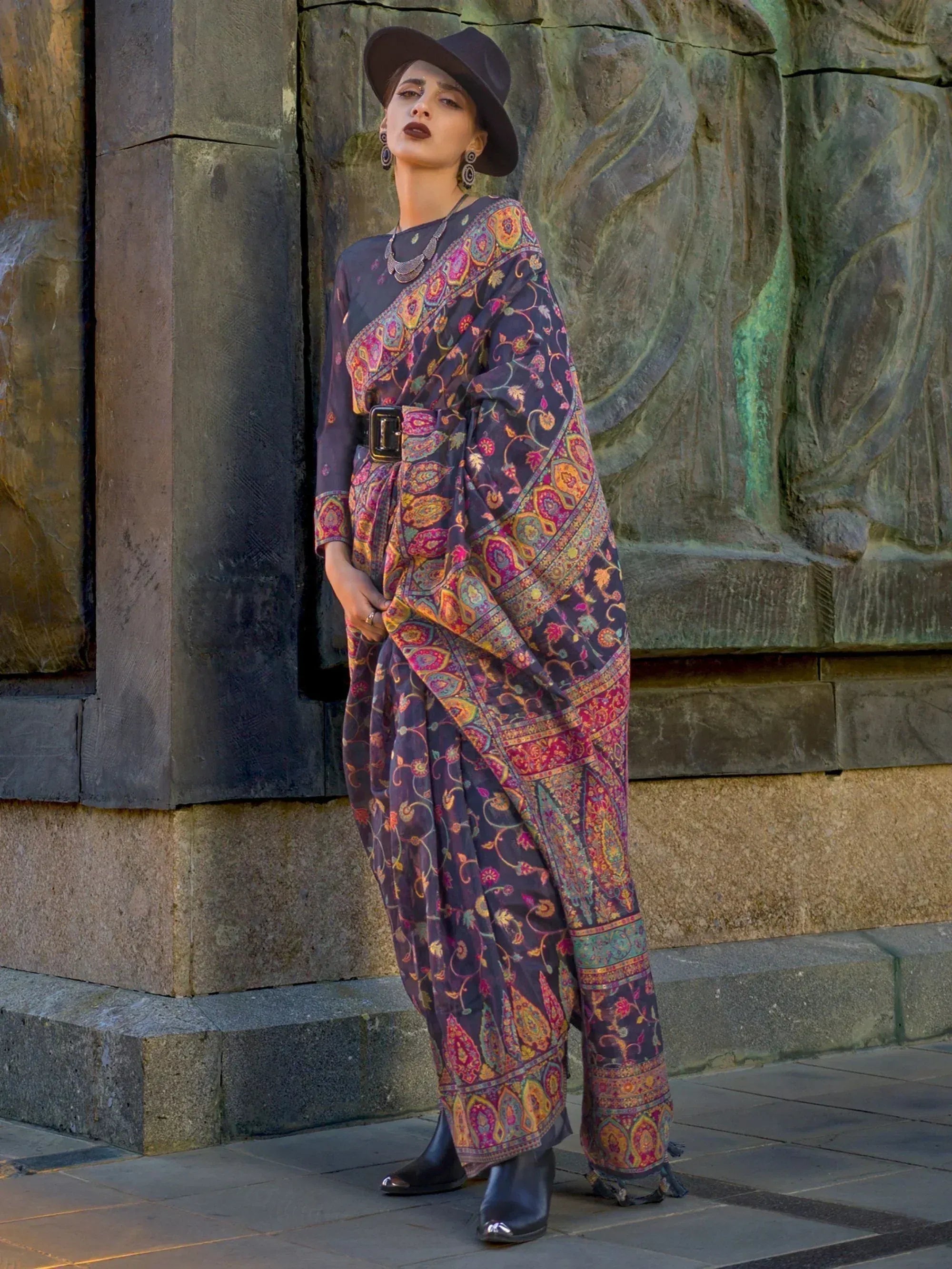 Woman in vibrant paisley print ethnic saree with black hat, styled for modern Indian fashion.