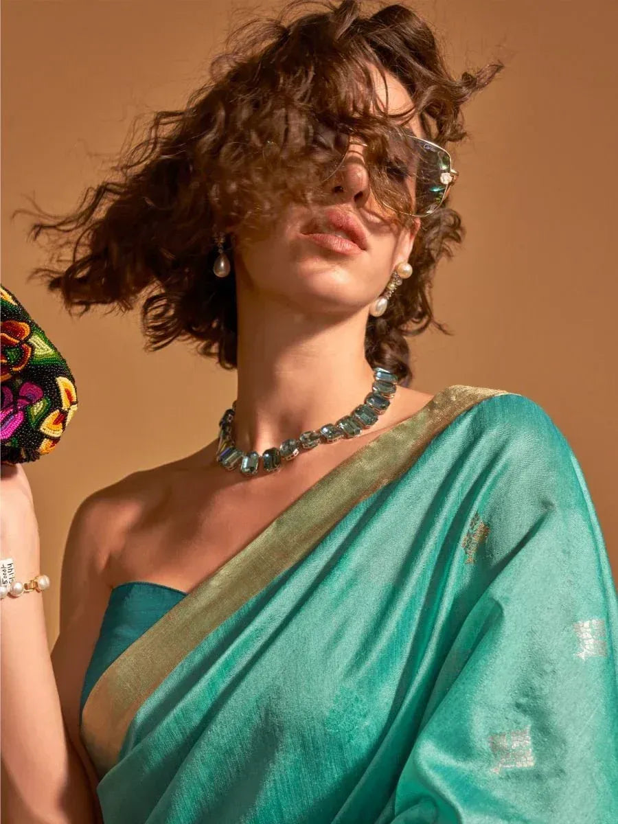 Woman in teal silk saree with gold border, pearl earrings, and statement necklace, styled with sunglasses