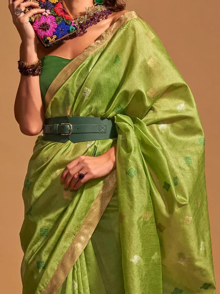 Green saree with gold border and floral clutch, styled with belt and jewelry