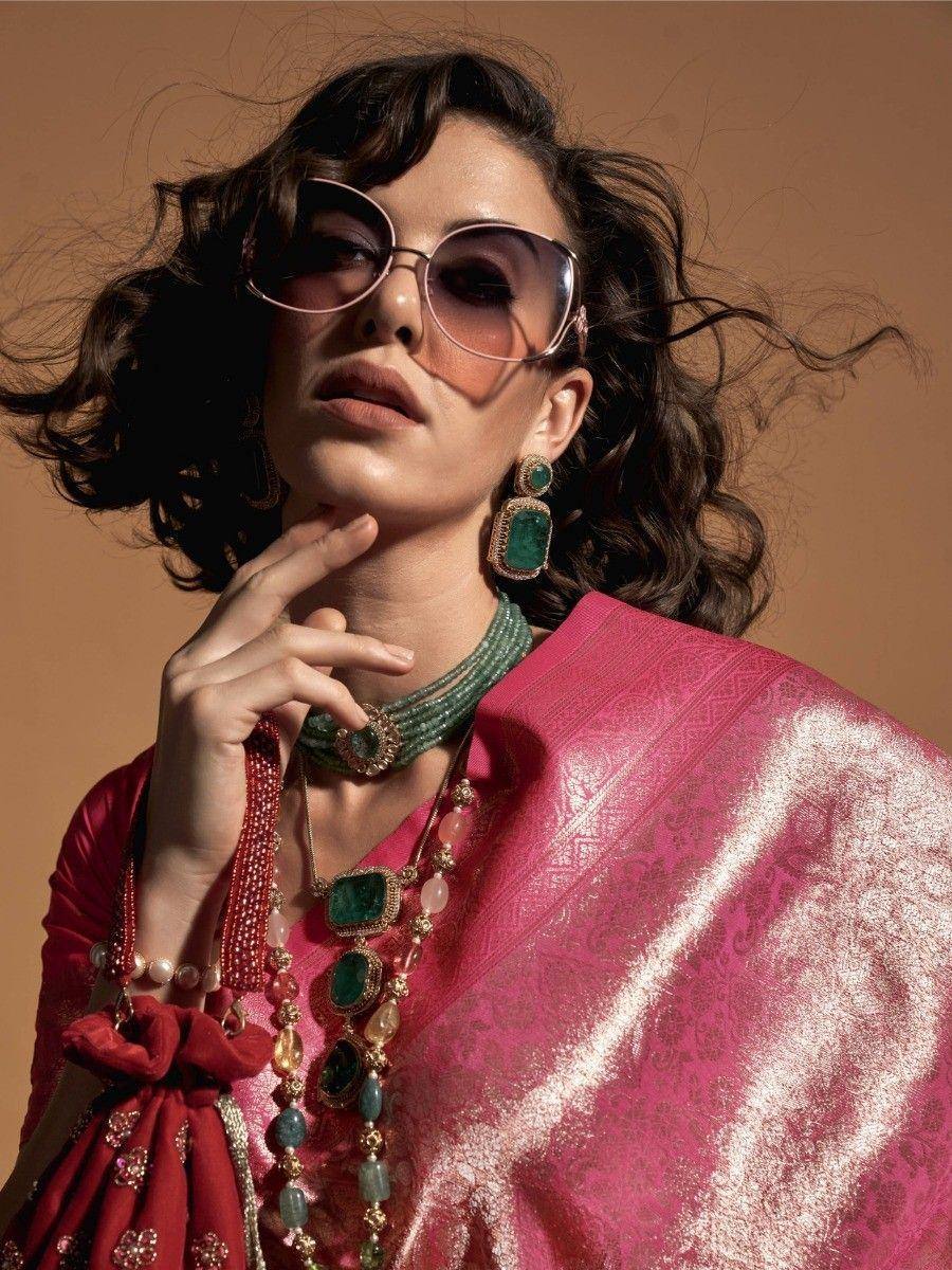 Woman in pink ethnic saree with emerald jewelry and sunglasses, styled for Indian fashion