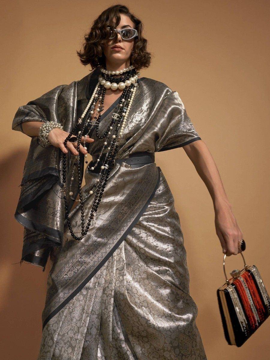 Stylish silver metallic saree with black border, layered pearl necklaces, and chic handbag for ethnic fashion