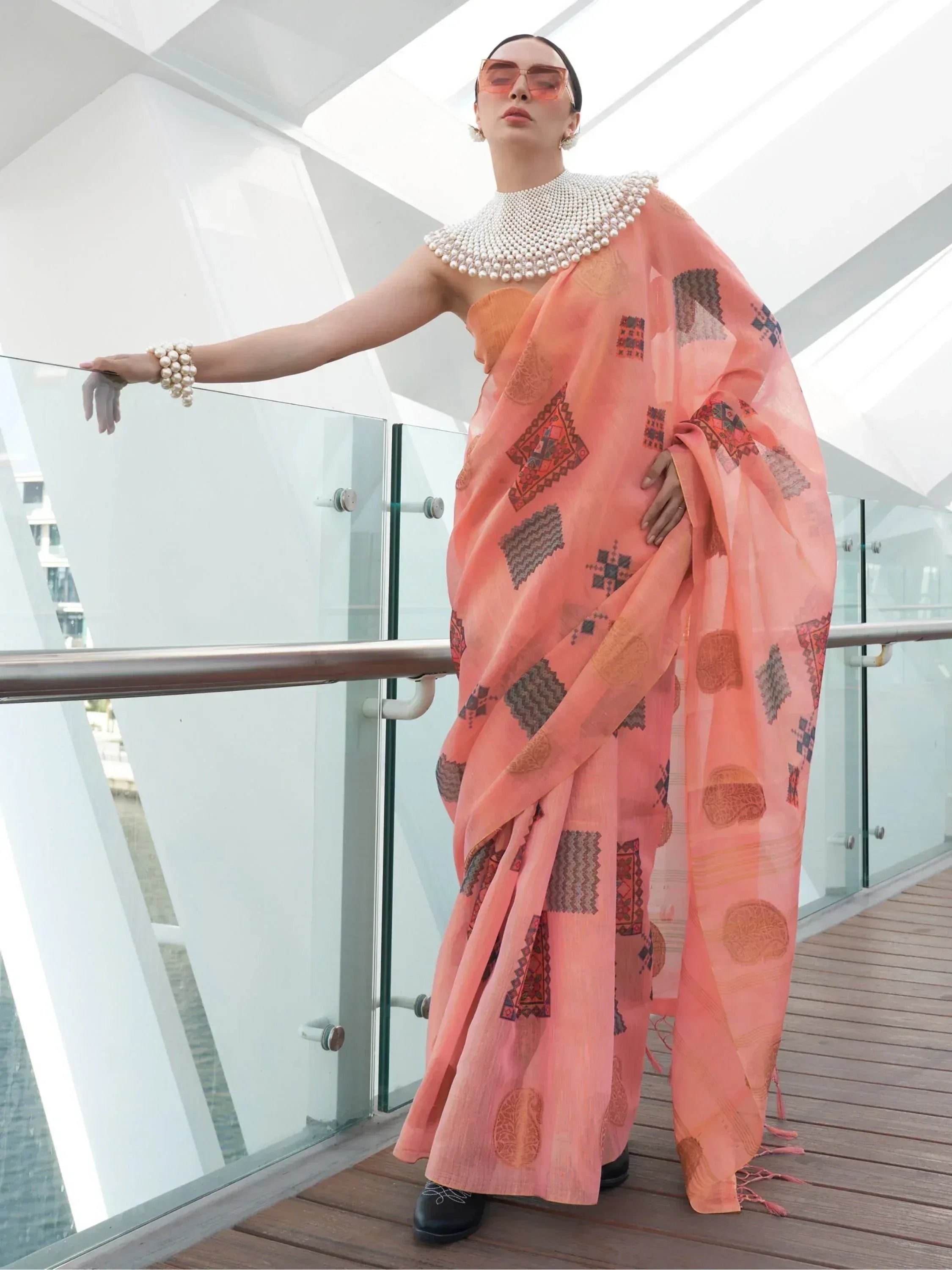 Peach printed saree with pearl embellished neckline, styled with sunglasses and pearl jewelry for ethnic wear
