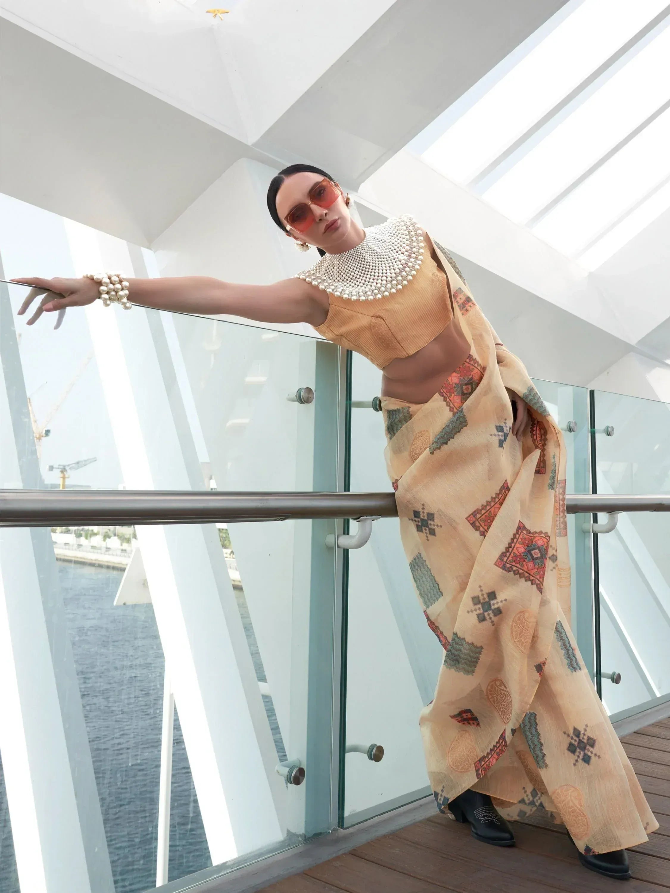Woman in ethnic saree with pearl embellished crop top, stylish sunglasses, and black boots on modern balcony