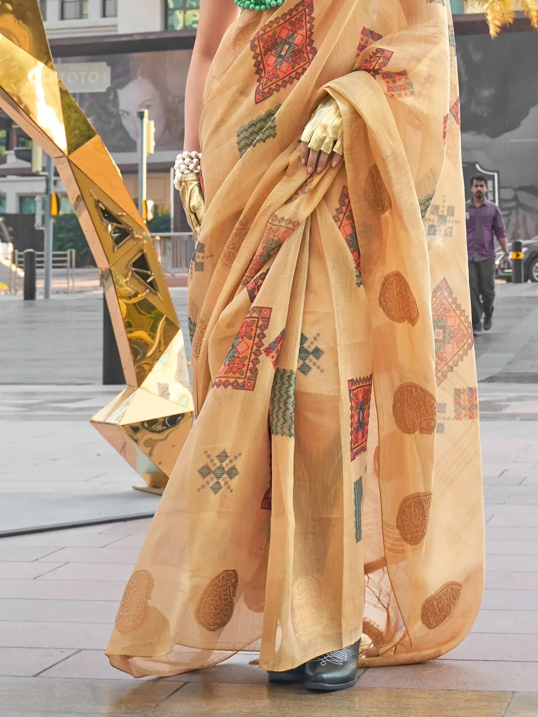 Woman in mustard yellow ethnic saree with geometric and paisley prints, paired with gold gloves and green beads
