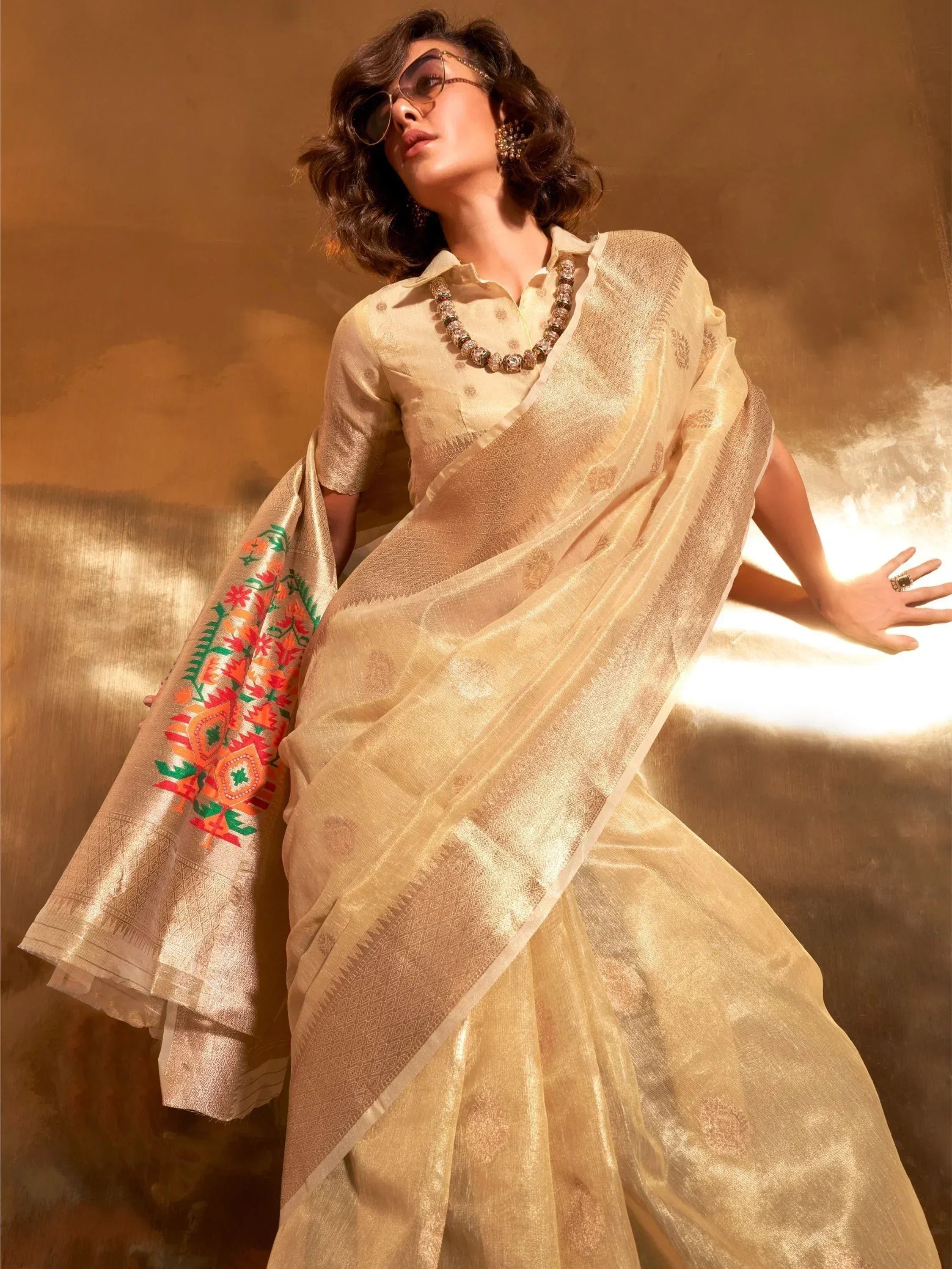 Elegant beige saree with colorful floral embroidery and gold patterns, styled with sunglasses and statement jewelry