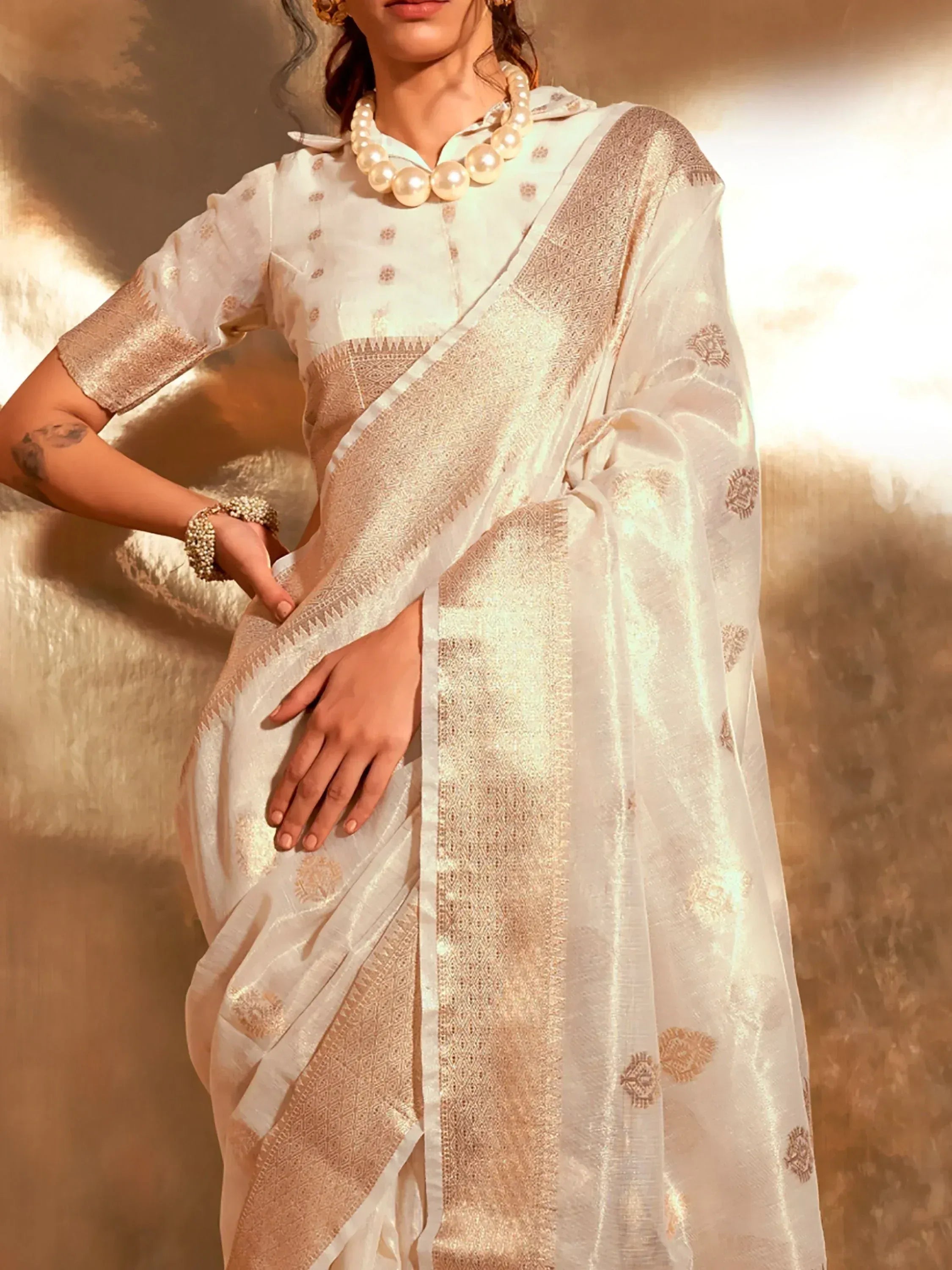 Elegant white saree with gold embroidery, paired with pearl jewelry for traditional Indian ethnic wear.