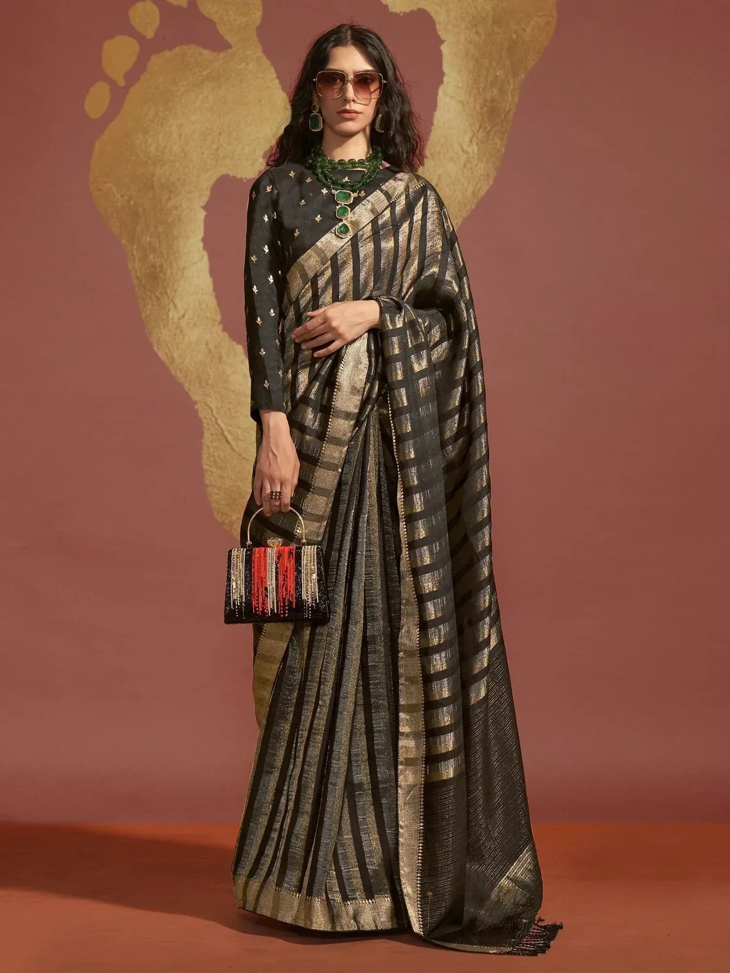 Black and gold striped saree with matching blouse, green jewelry, and beaded handbag for ethnic wear