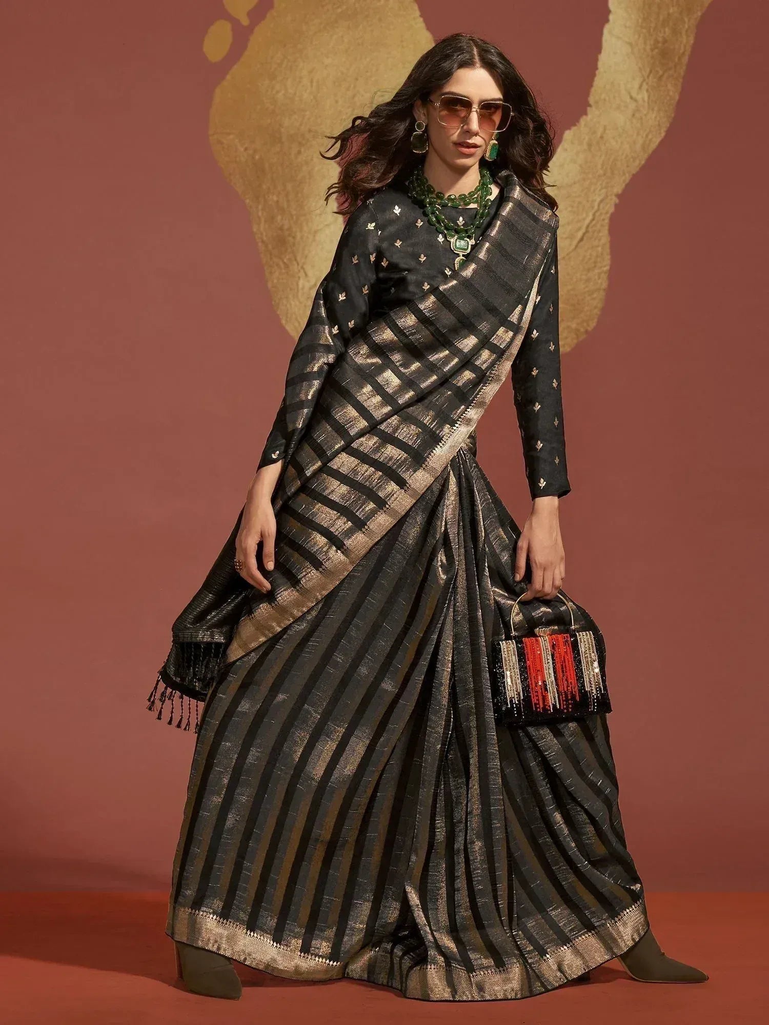 Black and gold striped ethnic saree with blouse, paired with green jewelry and clutch, perfect for Indian occasions