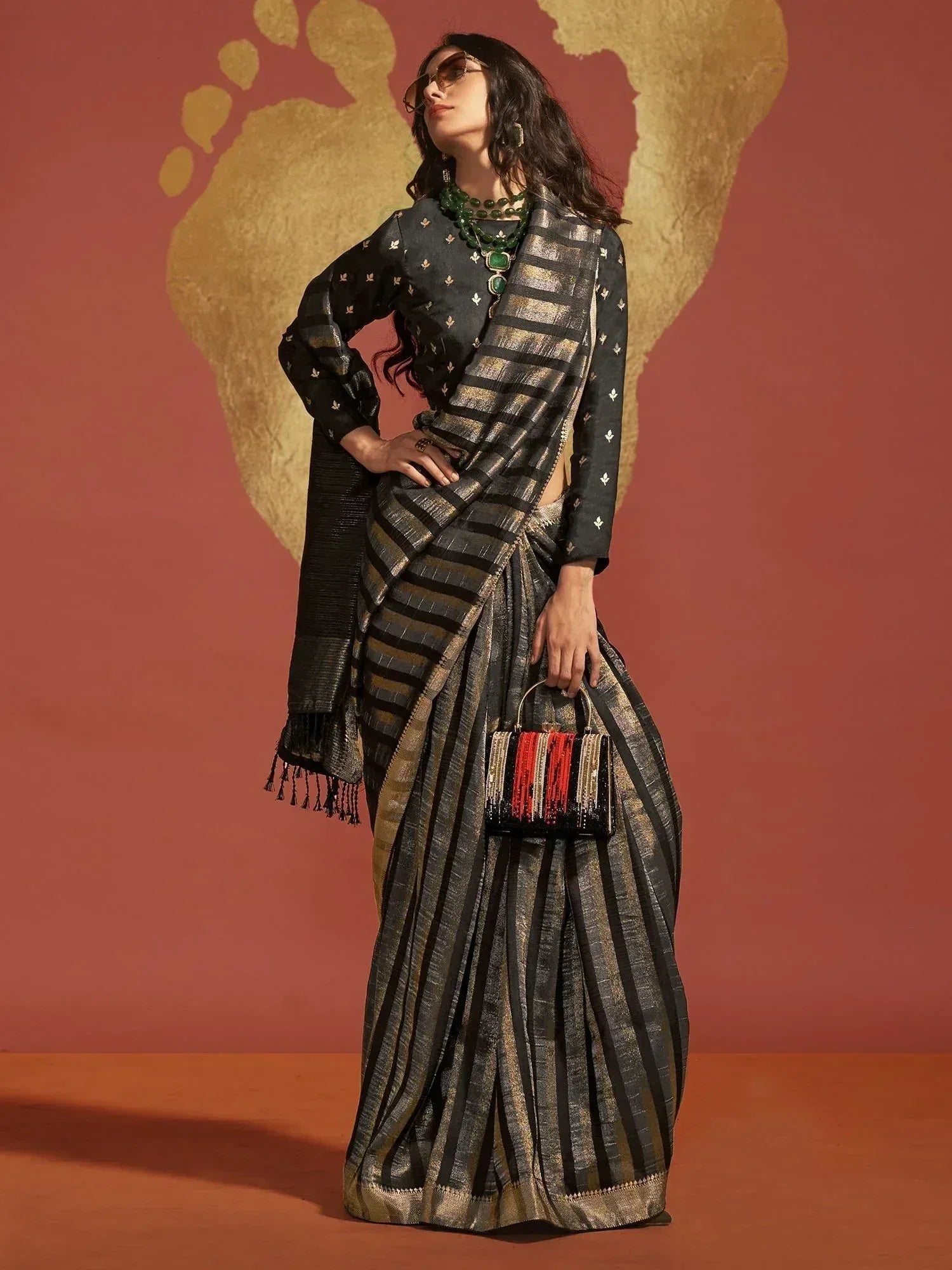 Black and gold striped saree with embroidered blouse, styled with green jewelry and fringe bag for ethnic wear