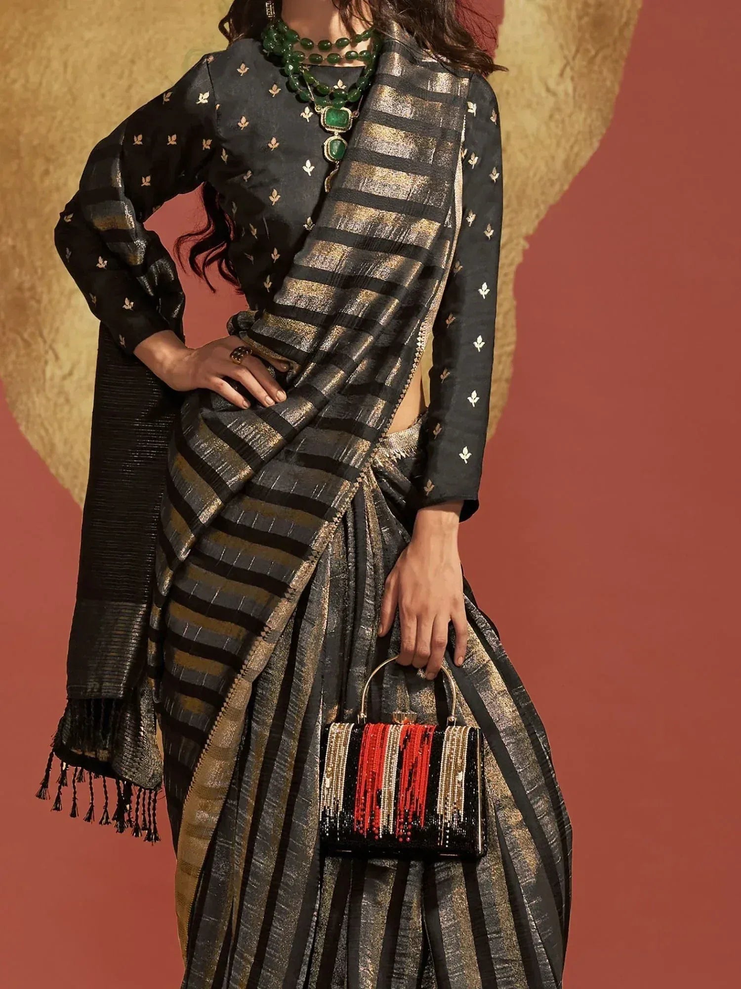 Black and gold striped saree with embroidered blouse, green necklace, and beaded clutch for ethnic wear