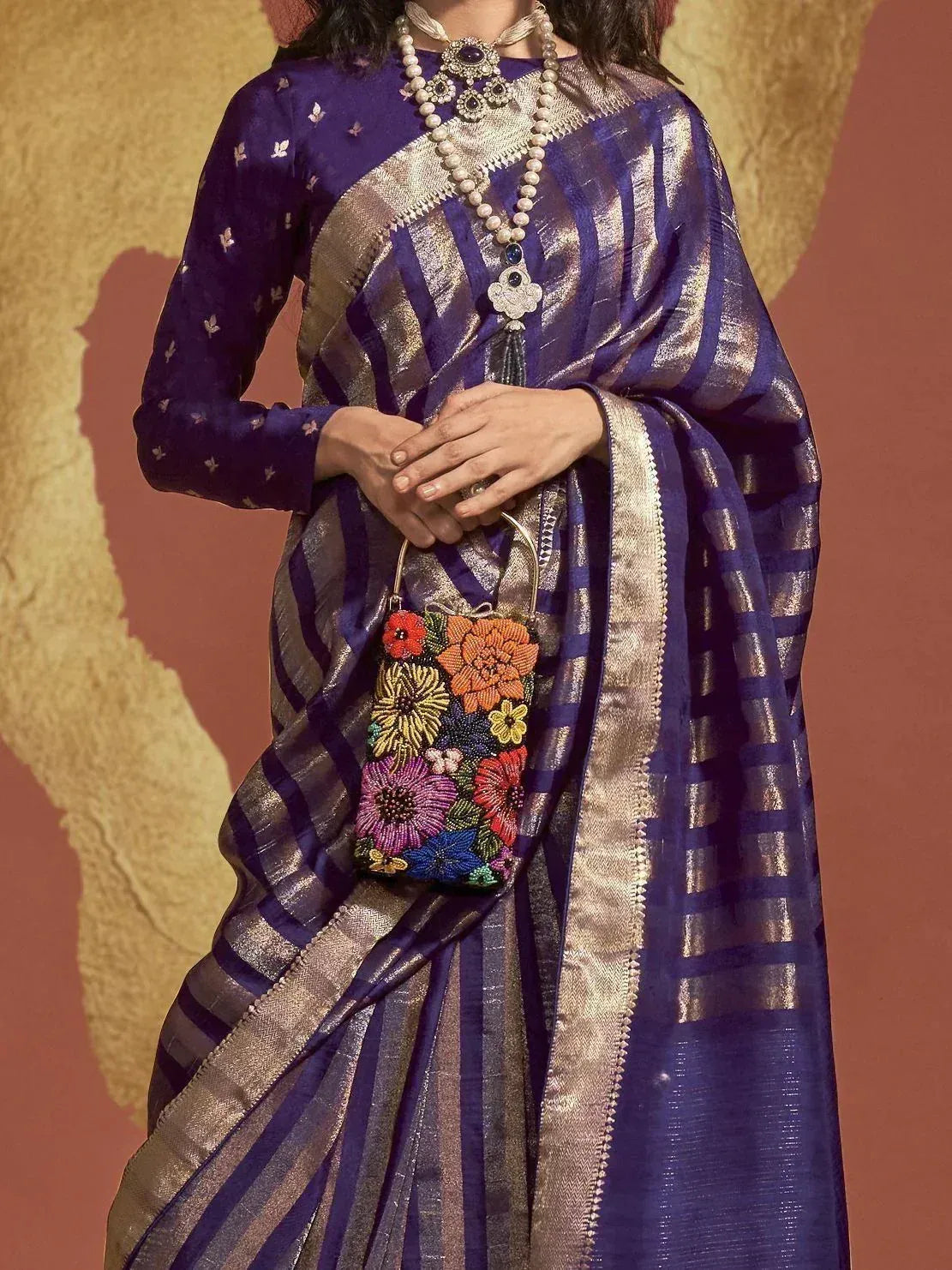 Purple and gold striped saree with floral embroidery, paired with beaded clutch and statement jewelry
