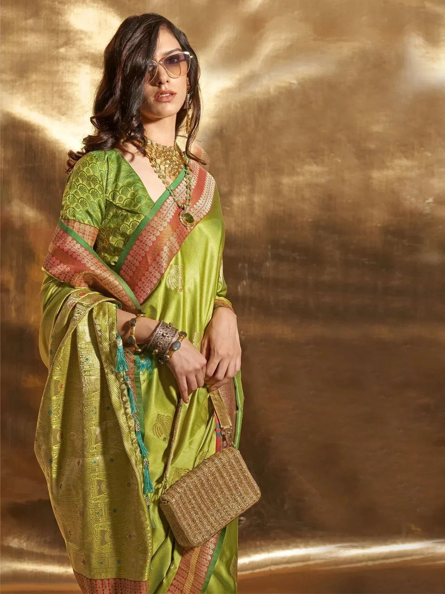 Green designer saree with gold embroidery, ethnic jewelry, and woven clutch for Indian festive wear