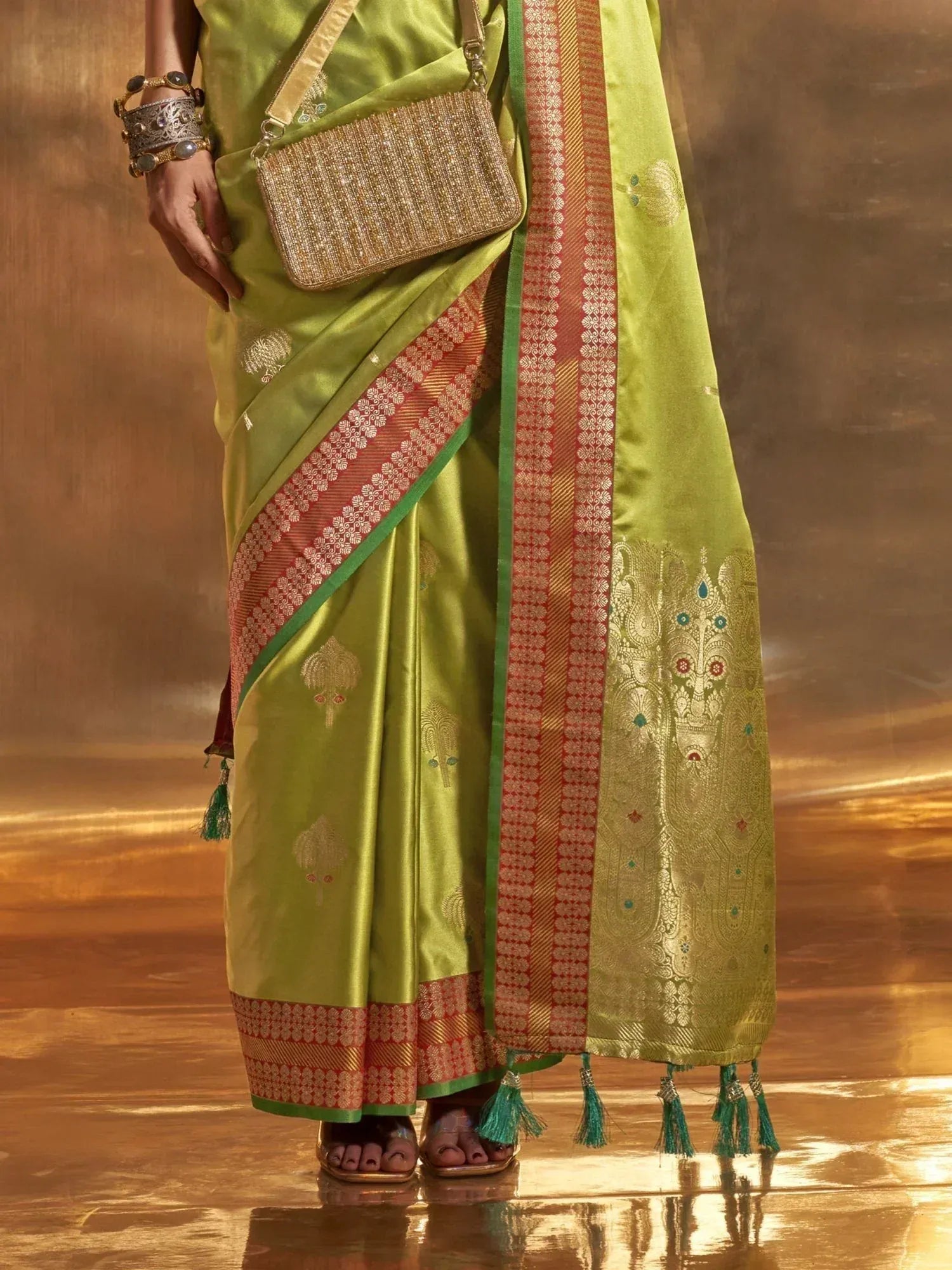 Lime green designer saree with gold peacock motifs, red border, and tassels, paired with ethnic jewelry and clutch.