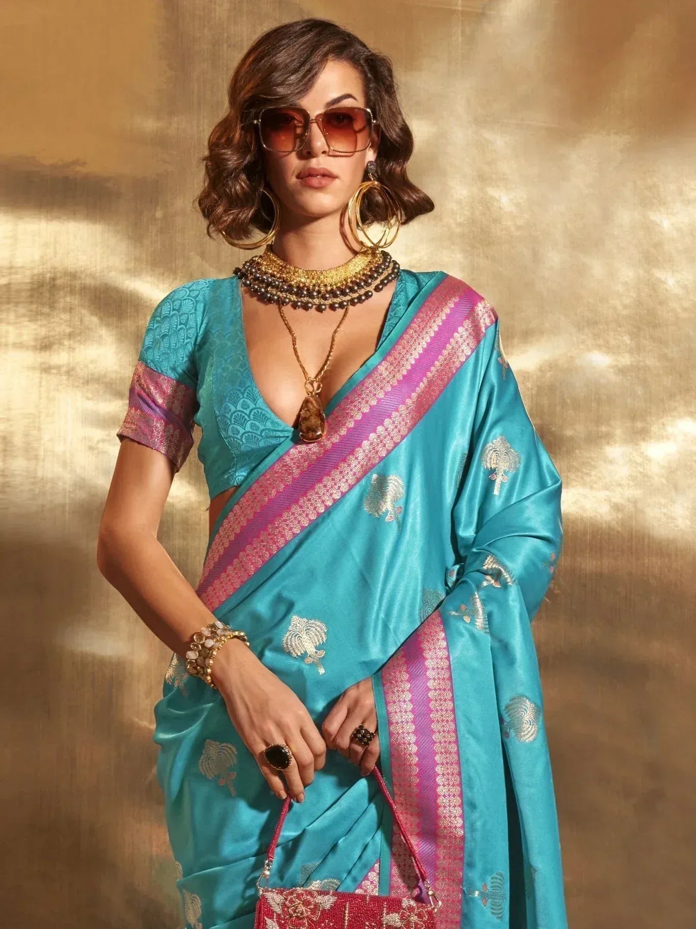 Turquoise designer saree with pink border and gold motifs, paired with statement jewelry for ethnic wear