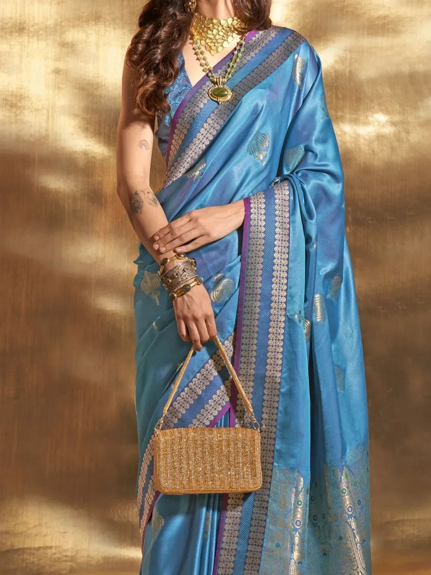 Blue silk saree with gold zari border, ethnic jewelry, and clutch for Indian festive wear