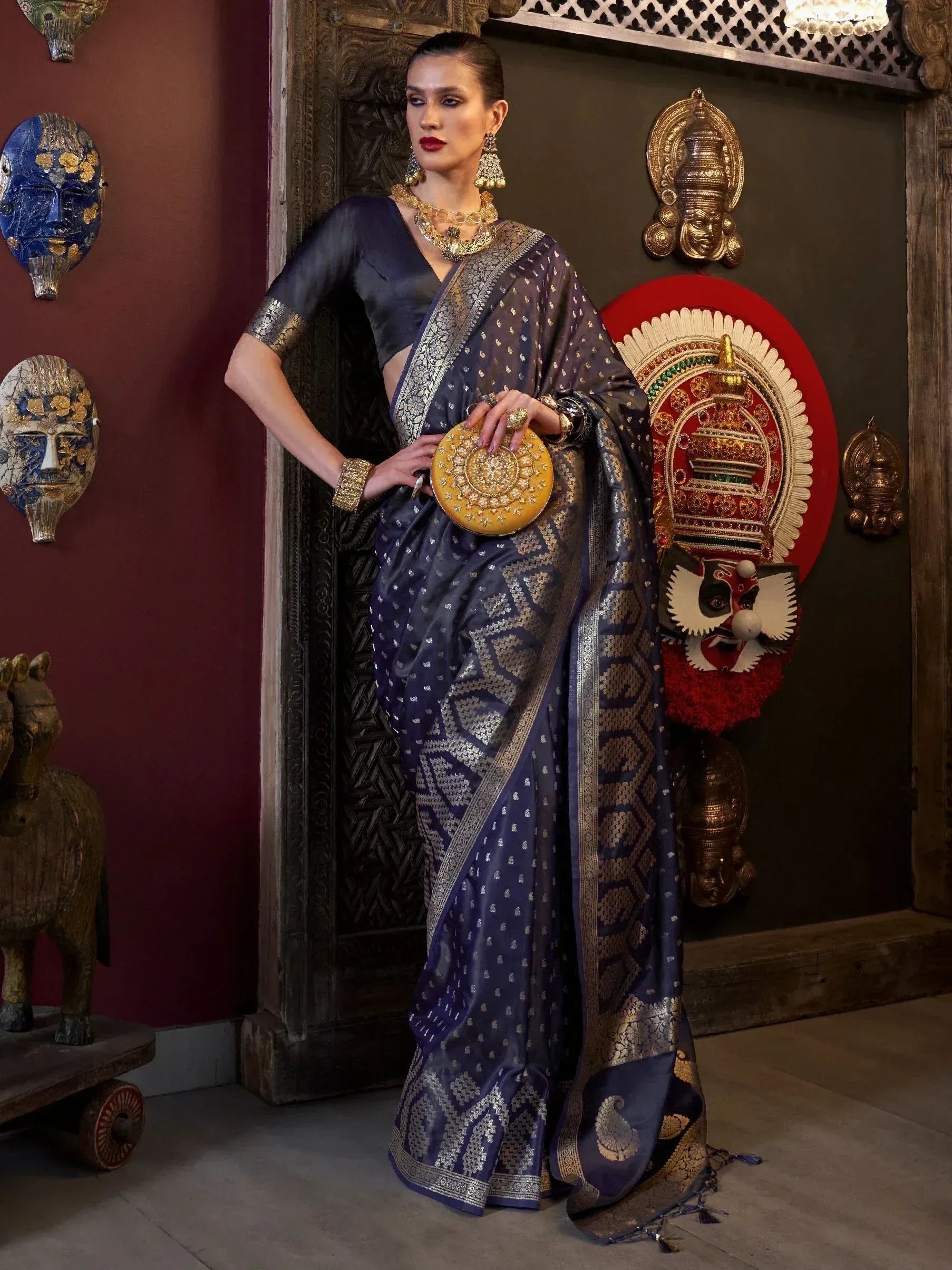 Elegant navy blue saree with gold zari work, paired with statement jewelry and a round clutch, perfect for Indian ethnic occasions.