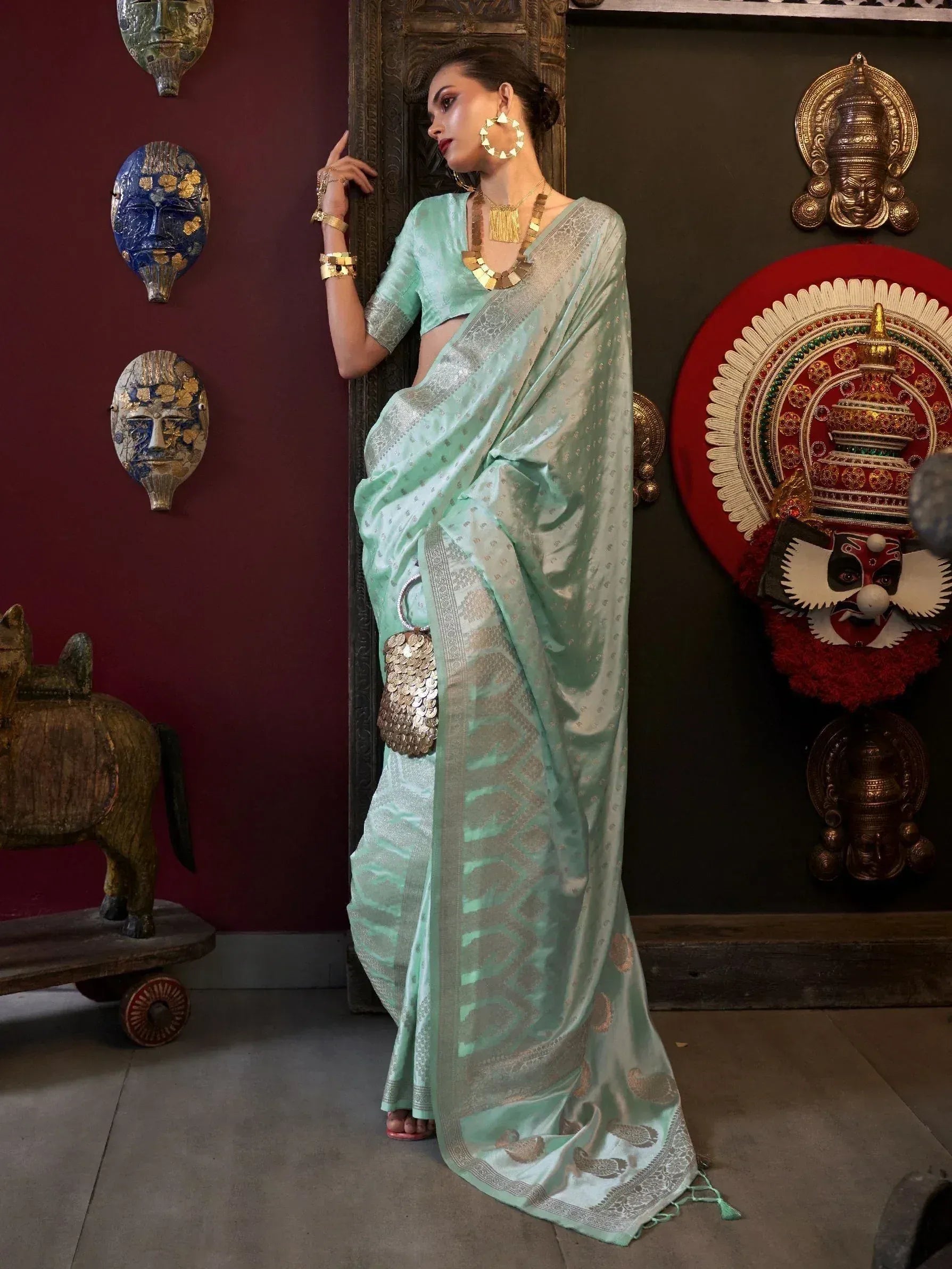 Mint green designer saree with gold zari work, paired with statement gold jewelry and a coin purse, perfect for ethnic occasions.
