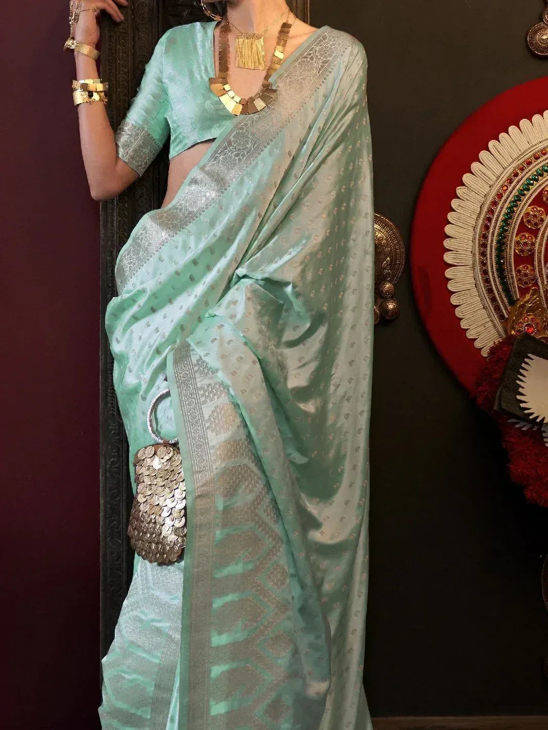 Mint green designer saree with silver zari border, paired with gold jewelry and sequin clutch for ethnic wear