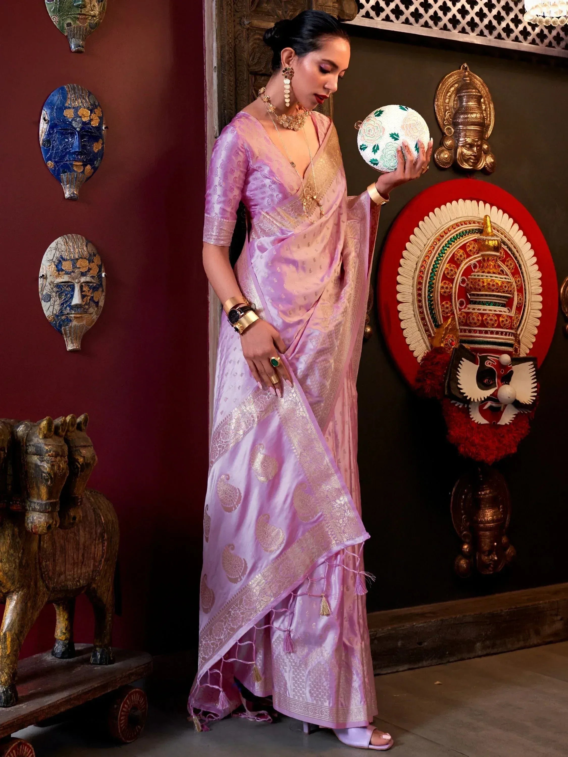 Elegant lavender silk saree with gold paisley print, paired with statement jewelry and a floral clutch, perfect for Indian ethnic occasions.