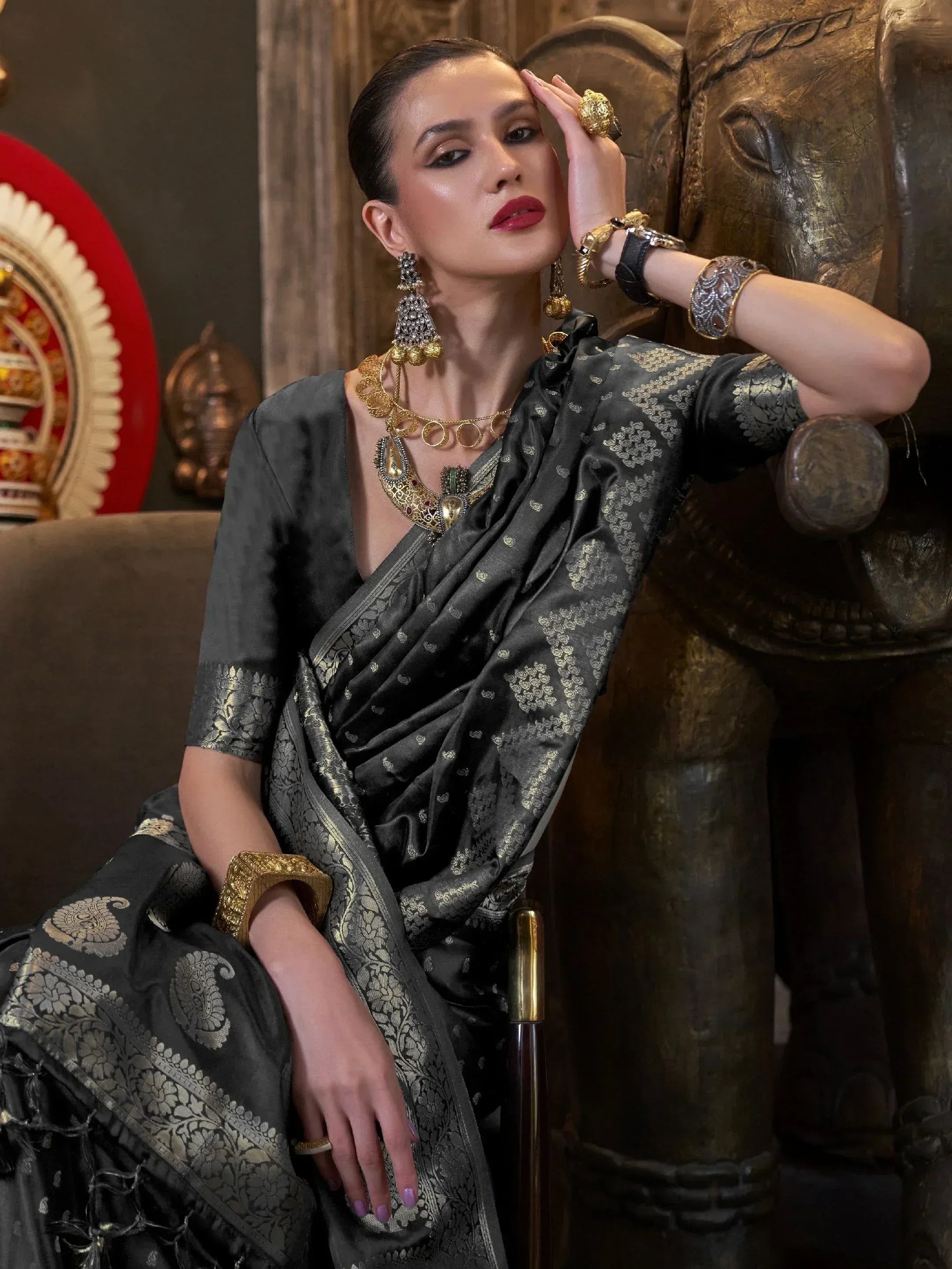 Elegant woman in black and gold designer saree with traditional Indian jewelry, posing beside carved elephant statue