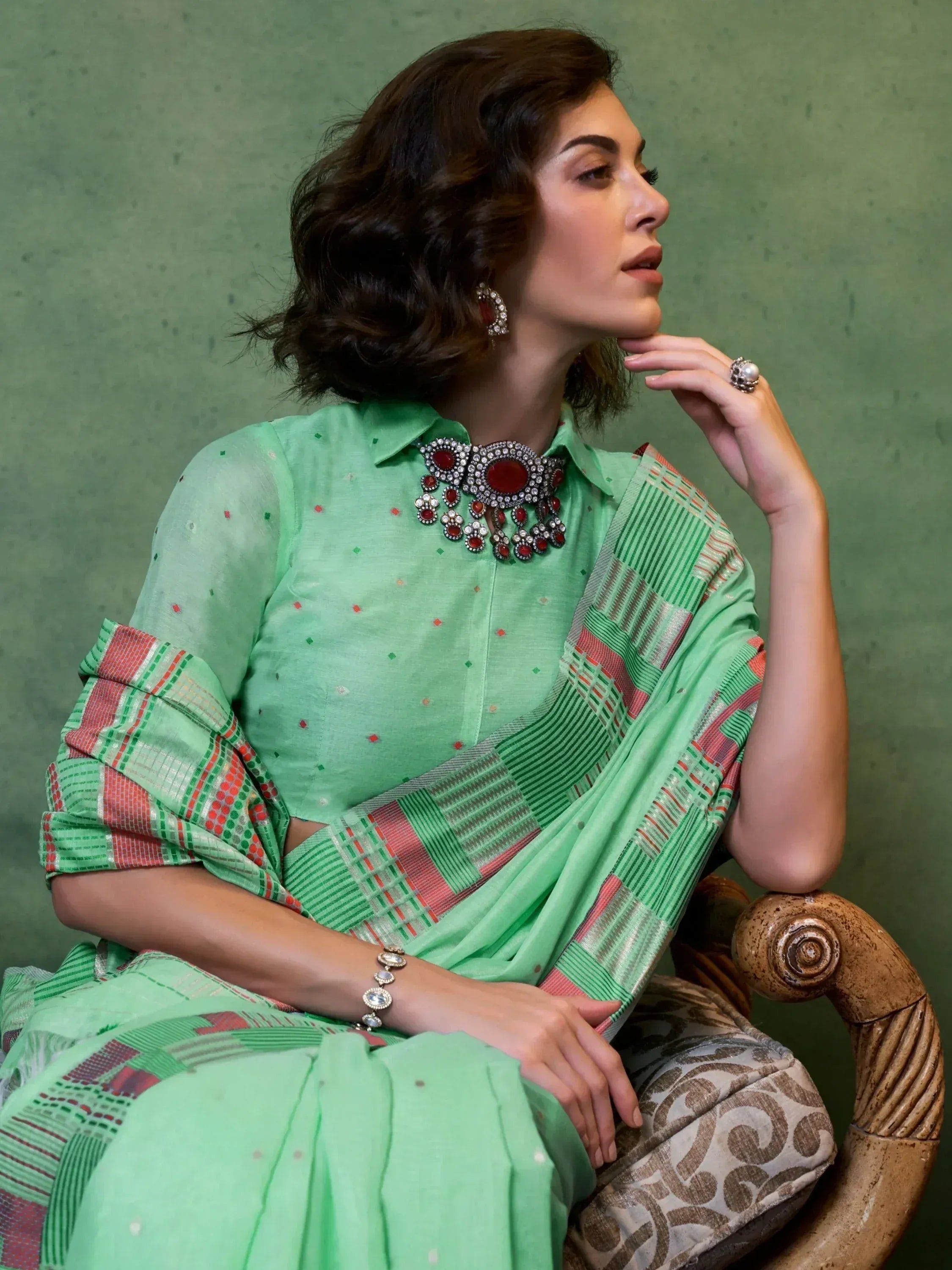 Woman in mint green ethnic saree with red and green geometric border, paired with statement jewelry